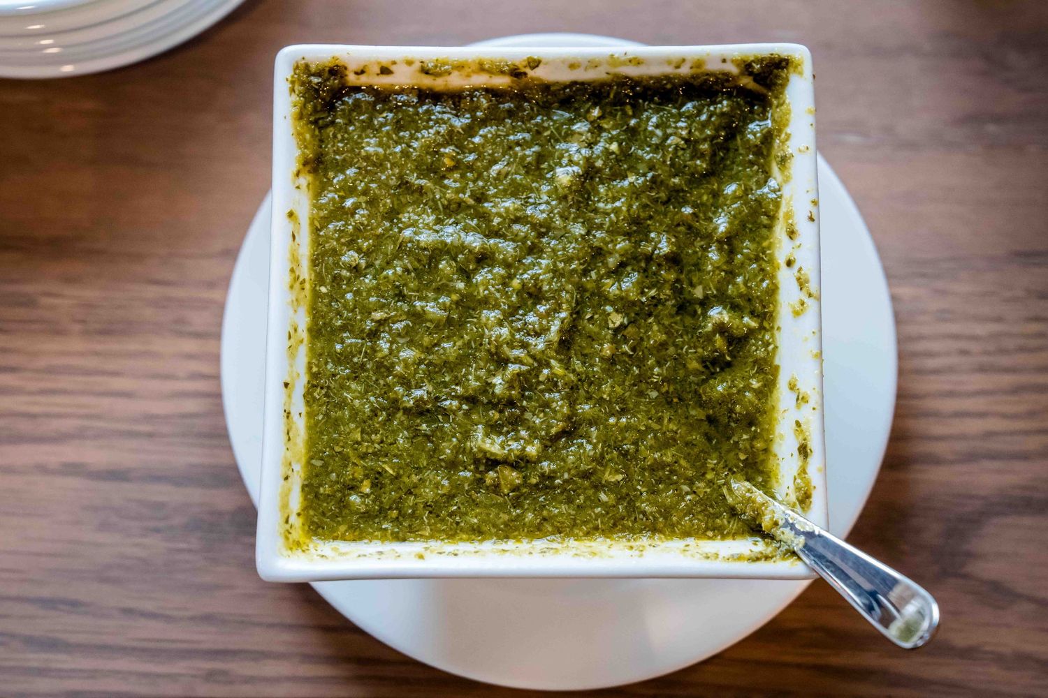 Square white dish filled with vibrant green pesto sauce, served on a white plate with a spoon.