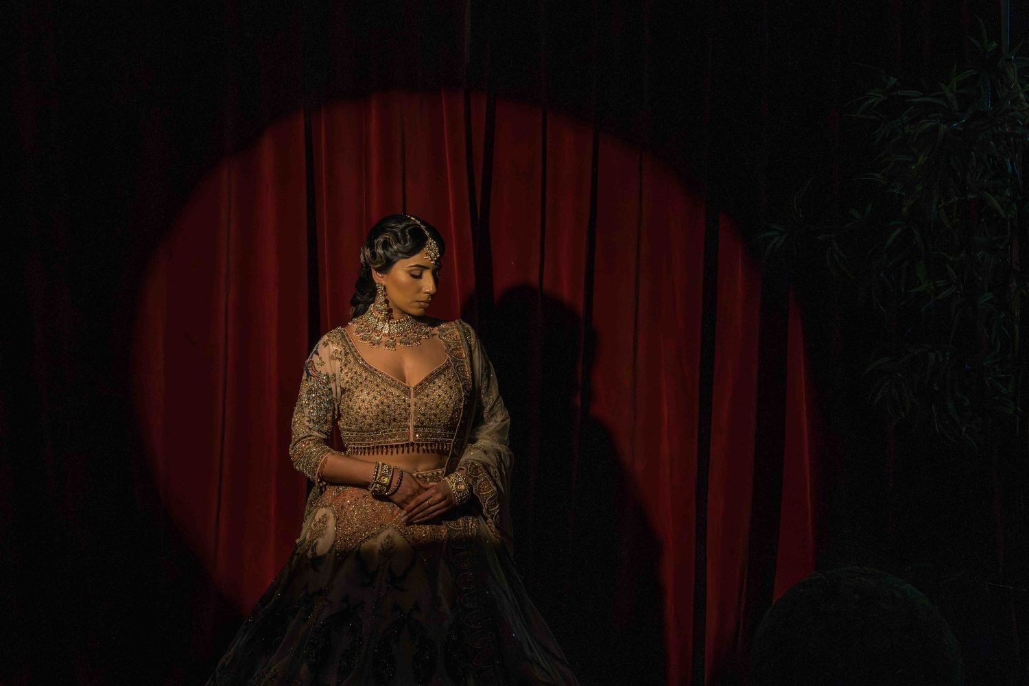 A person in an elegant lace dress sits illuminated by a dramatic red spotlight against dark curtains.