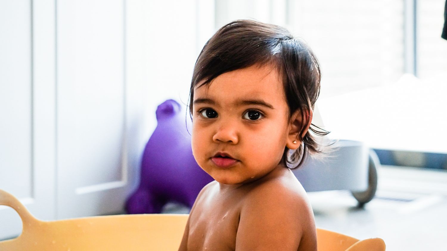 Toddler close-up portraits with purple balloon in bright white room.