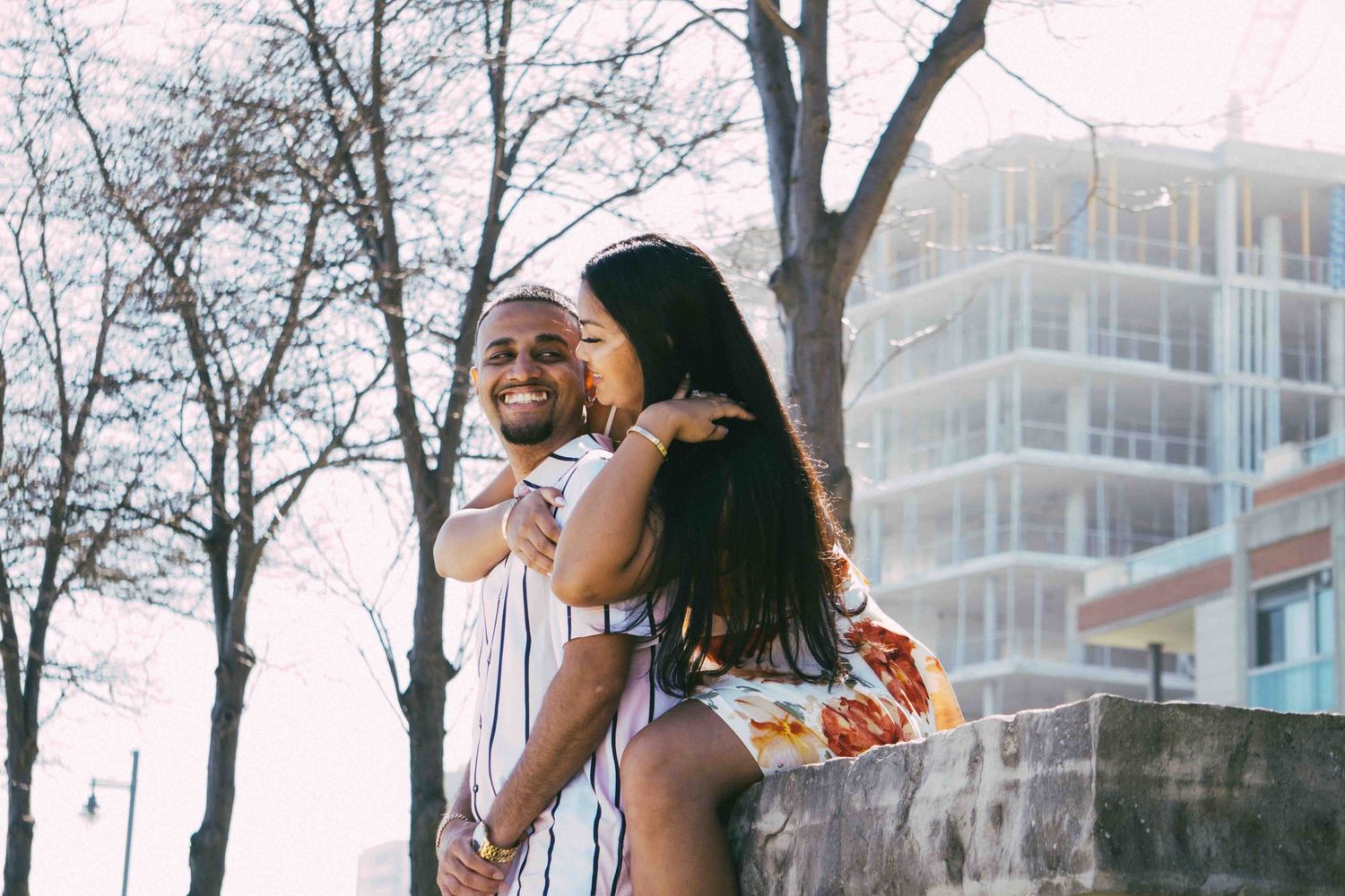 Couple walking together on a tree-lined path with buildings in the background.