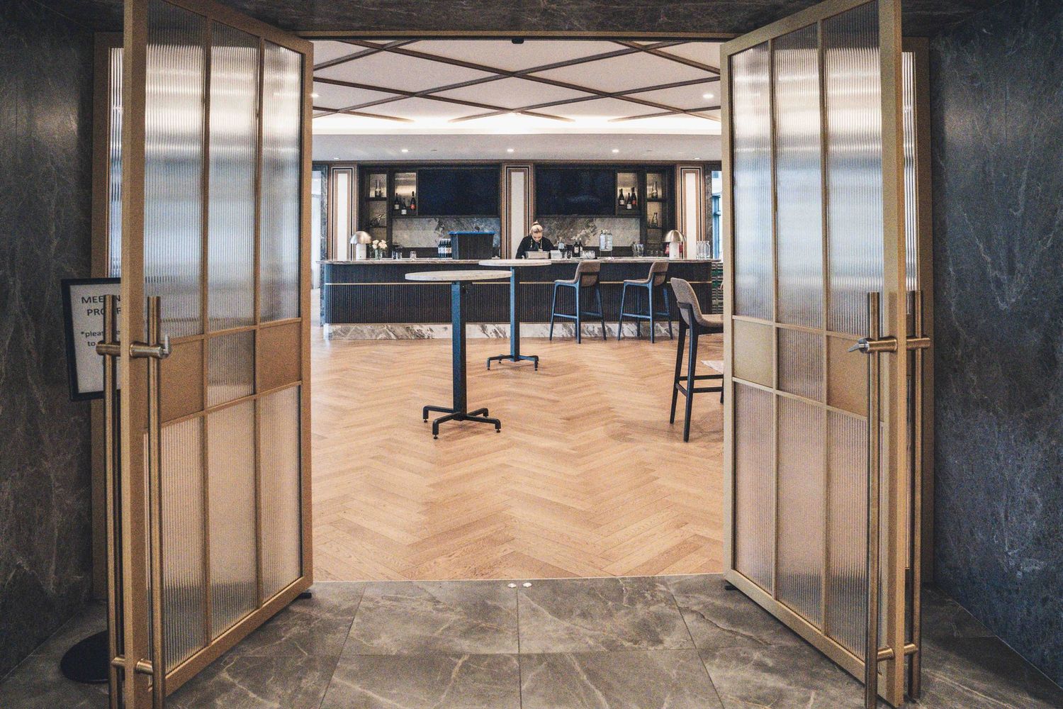 Elegant restaurant entrance with open gold-framed glass doors revealing a modern interior with herringbone wood floors.