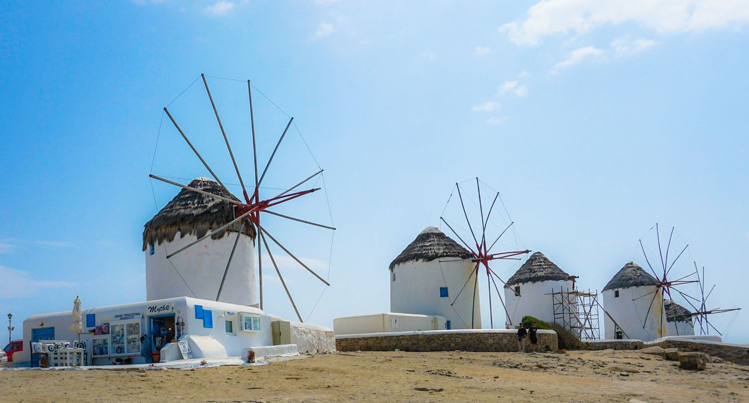Row of traditional windmills on hilltop against blue sky.