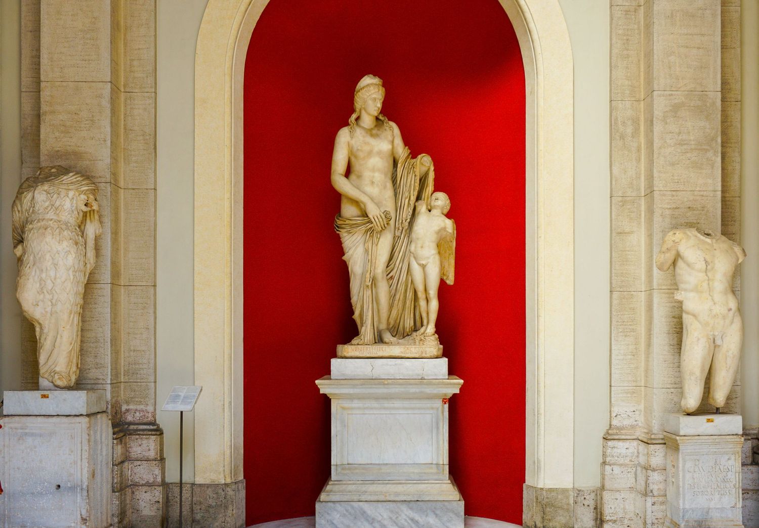 Classical marble statues displayed in museum alcoves with dramatic red backdrop highlighting central sculpture.