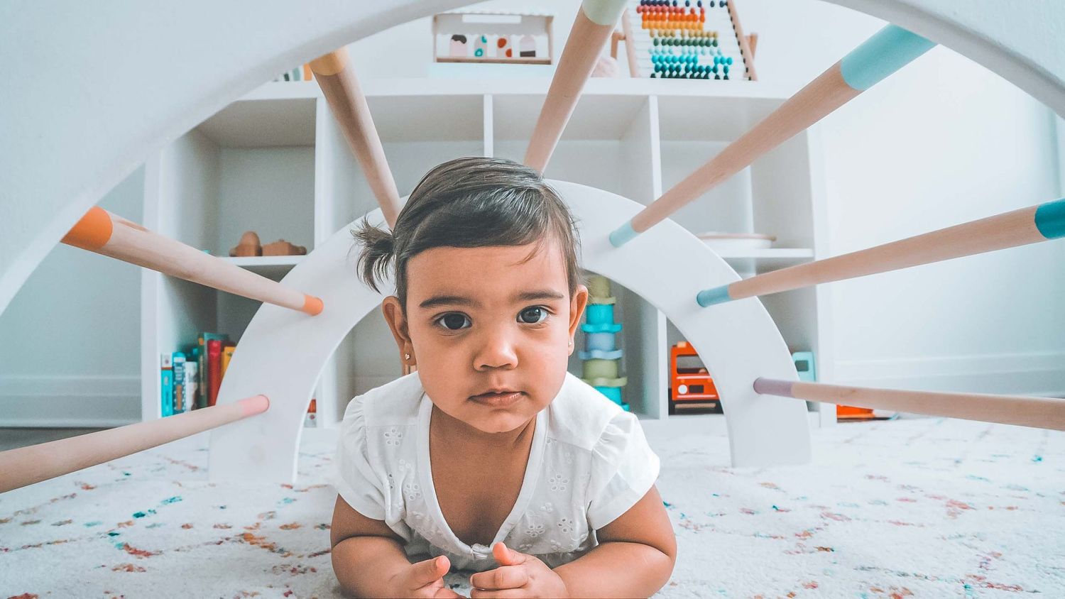 Small child lying on floor with colorful wooden sticks arranged in a star pattern behind them.