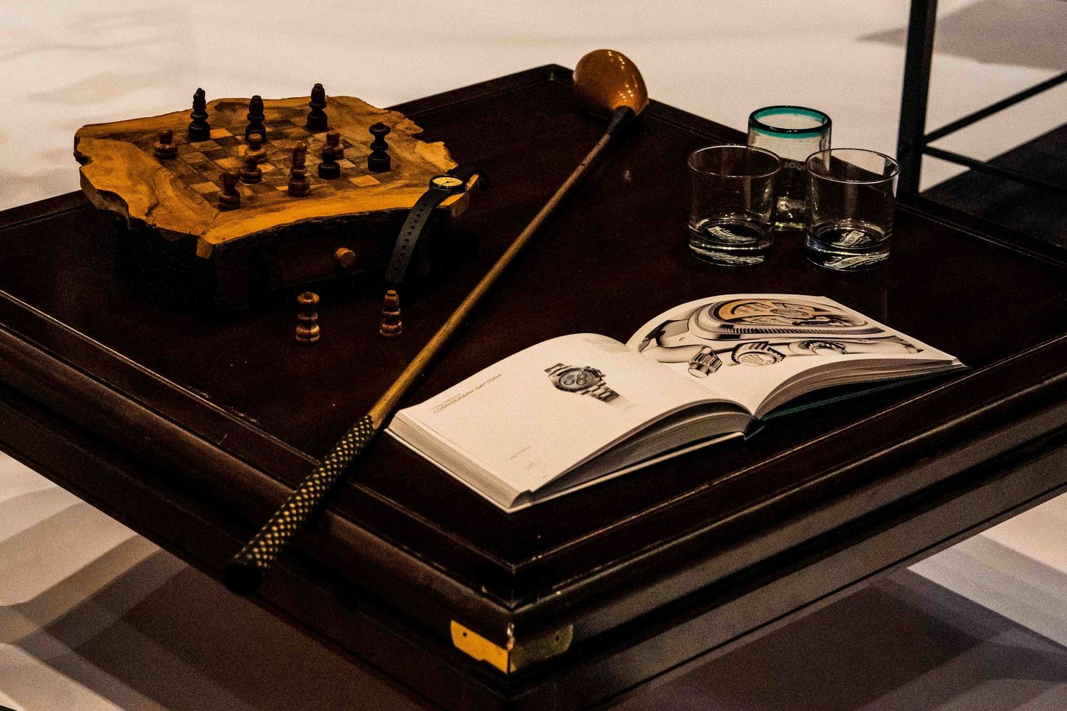 A vintage chess set sits beside an open book and magnifying glass on a dark wooden desk.