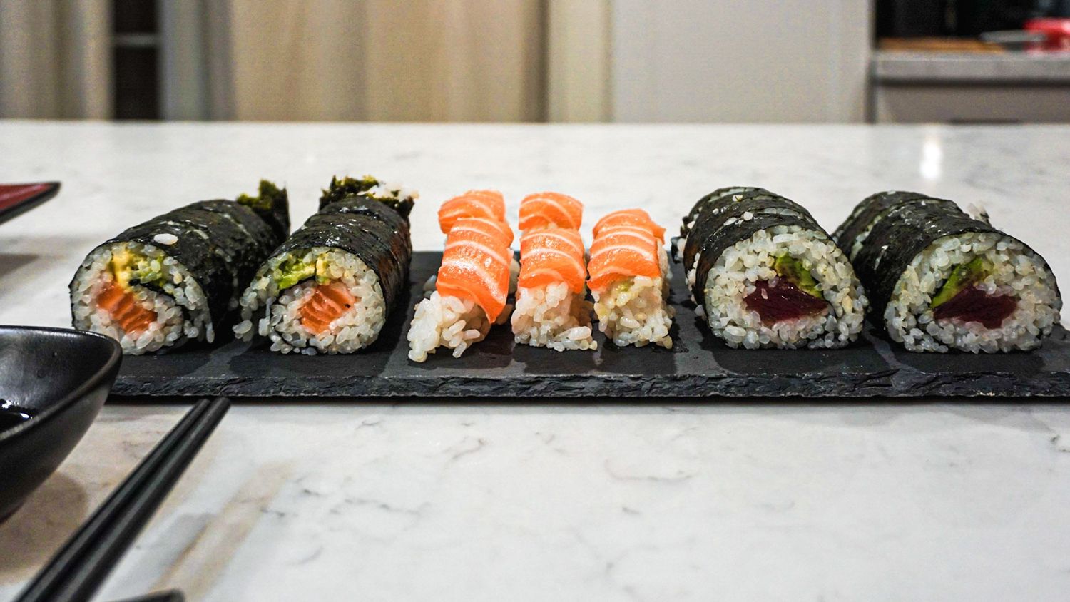 Assorted sushi rolls arranged in neat rows on a white serving platter.