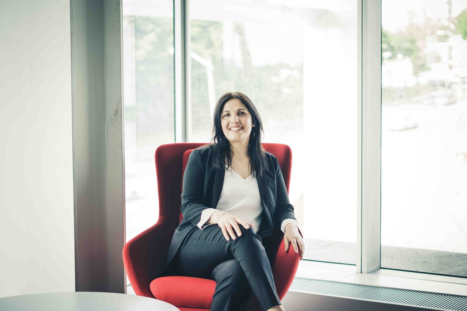 Business professional seated in modern office with bright windows and red chair.