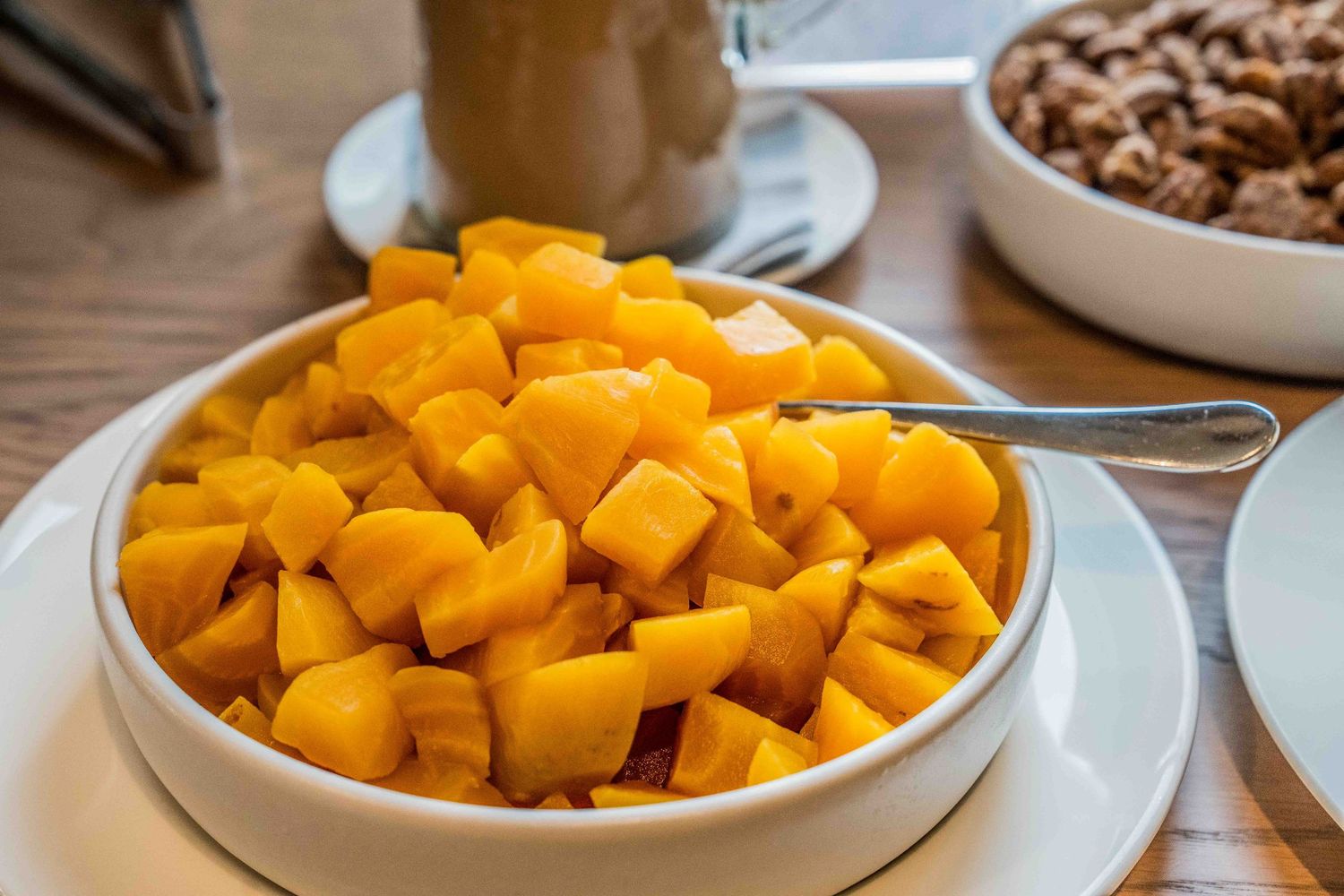 Bowl of fresh diced mango chunks served with a spoon on a white plate at a restaurant.
