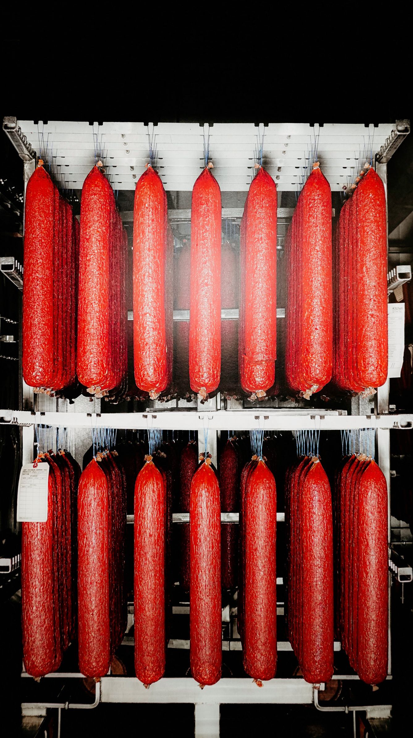 Two rows of bright red sausages hanging in industrial processing facility.