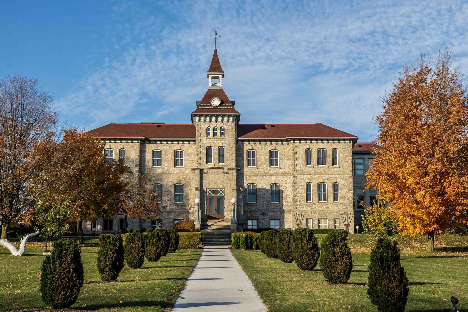 Historic institutional building with symmetrical architecture and autumn trees along a walkway.