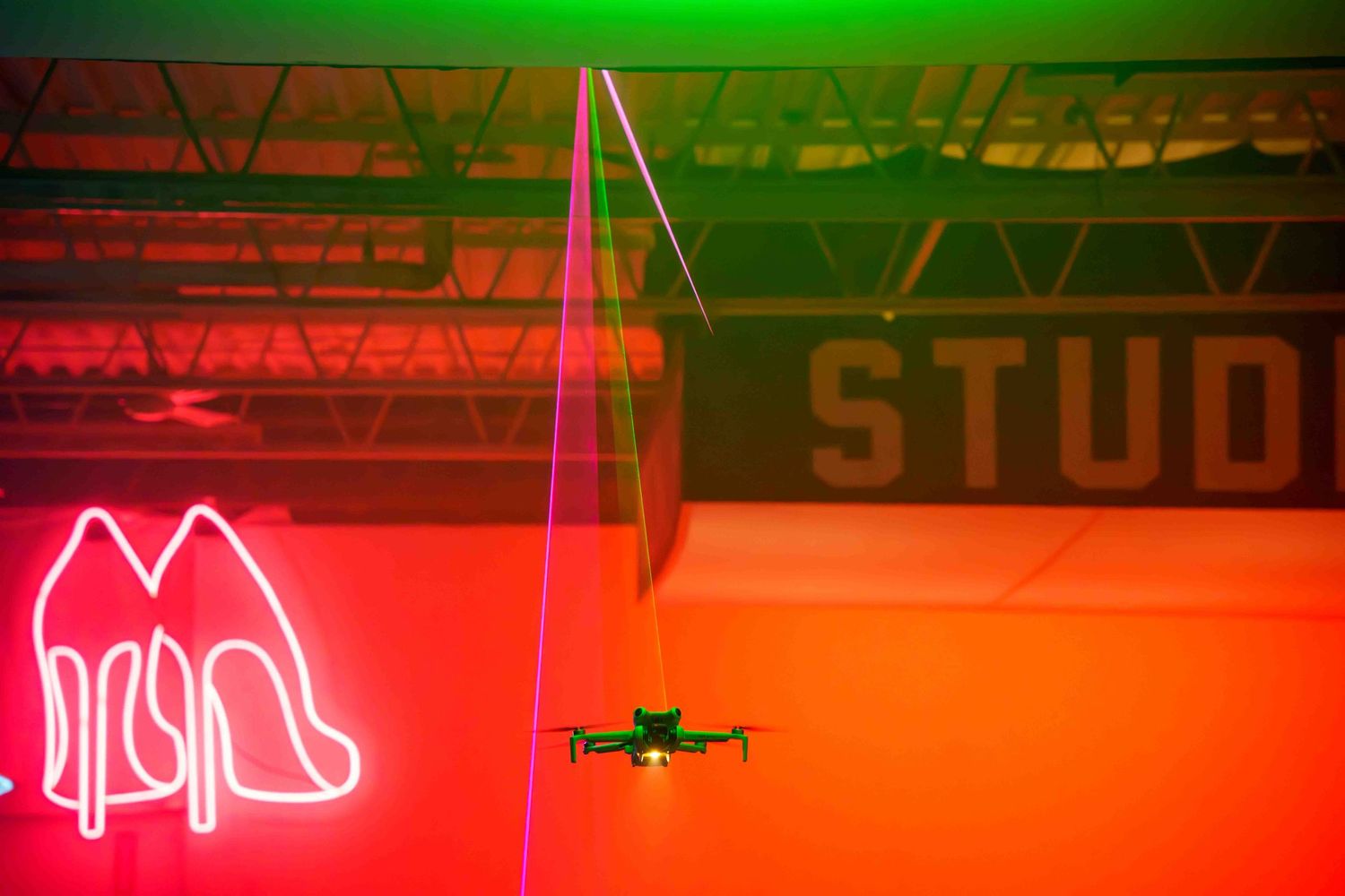 A drone flies past neon signs in a studio bathed in red and green lighting.