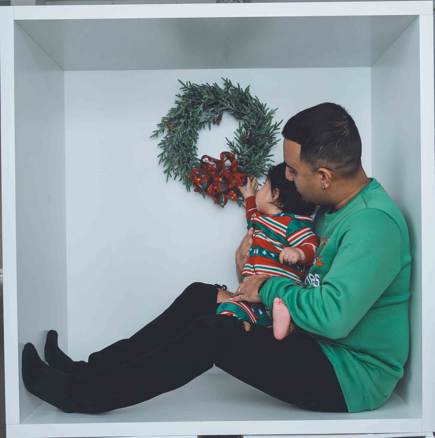 Family members in festive green sweaters interacting in a white studio space.