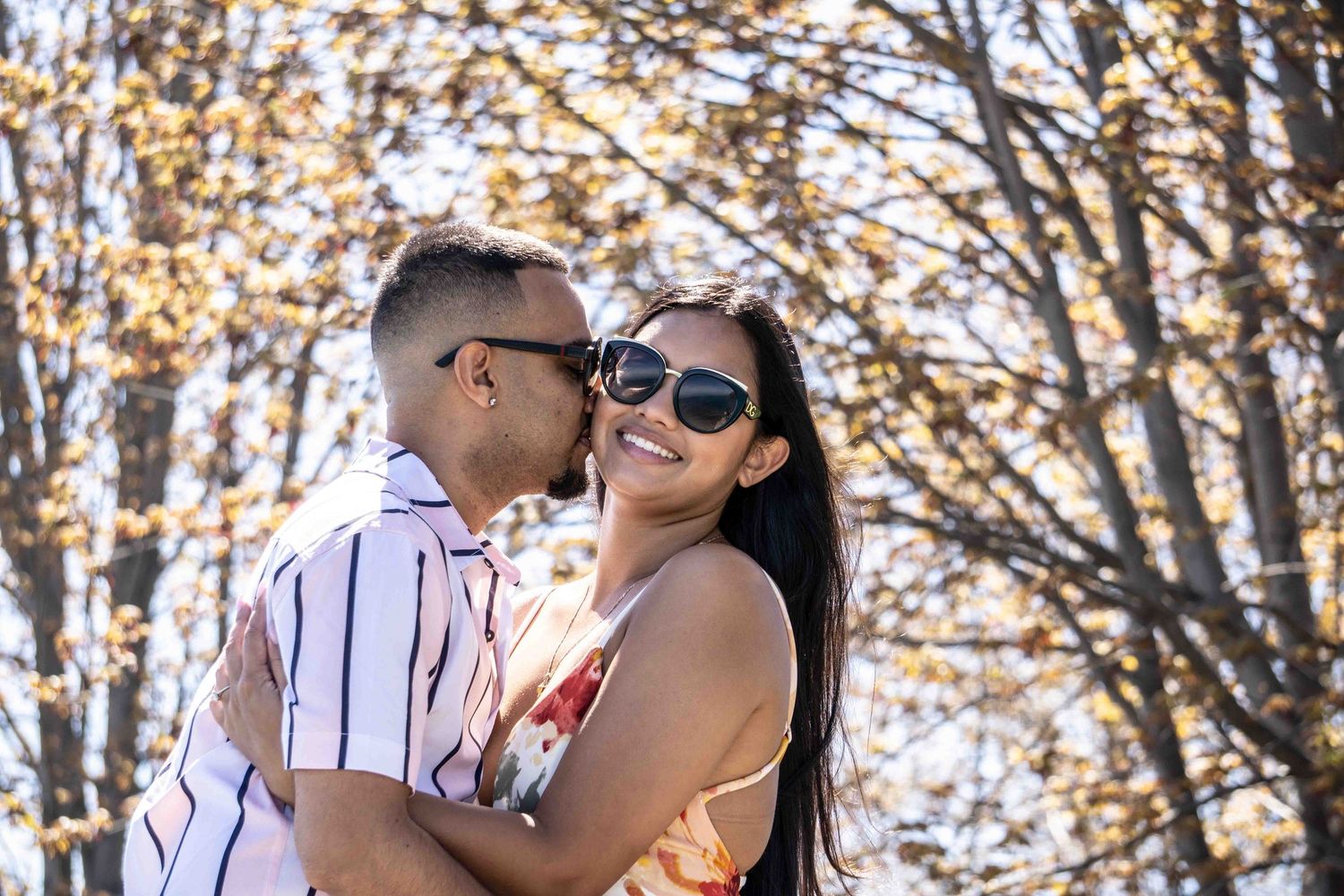 A romantic couple shares a tender moment among autumn trees in a park setting.