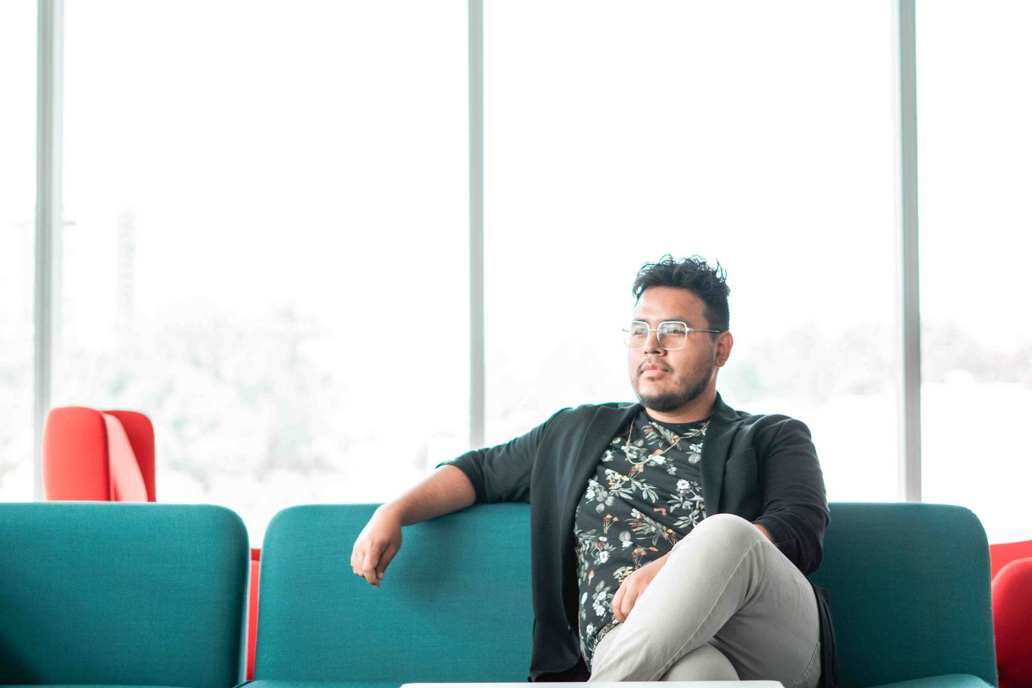 Professional relaxing on teal couch in modern office setting.