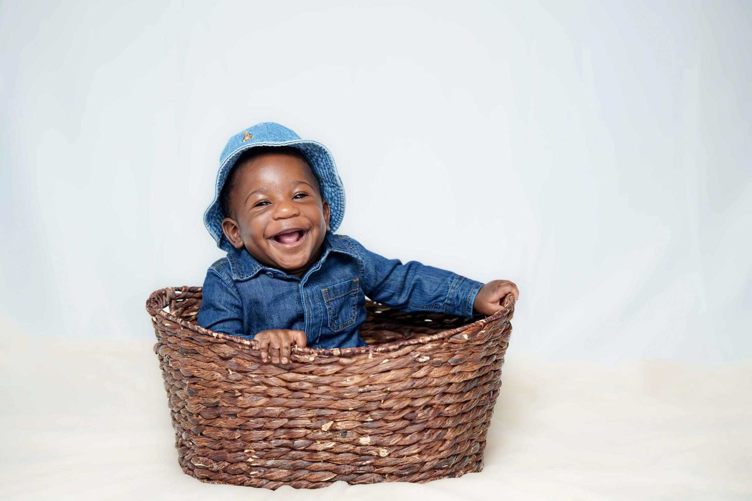 Happy child lying in brown woven basket wearing denim outfit.