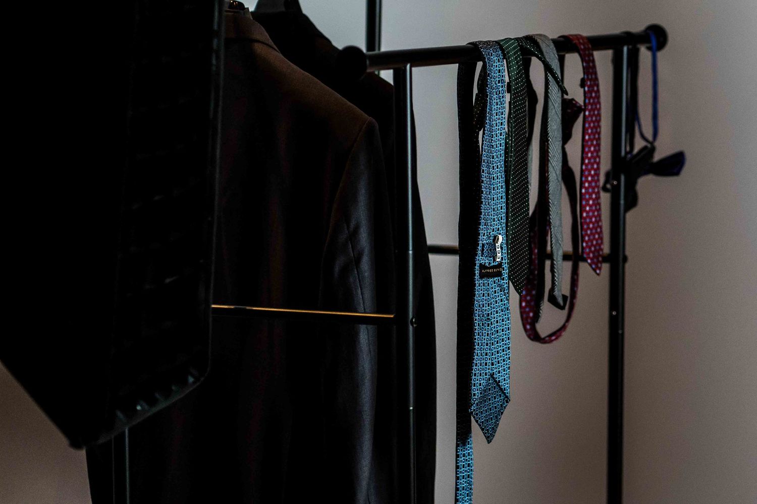 A row of colorful neckties hanging neatly on a black closet rack against a white wall.