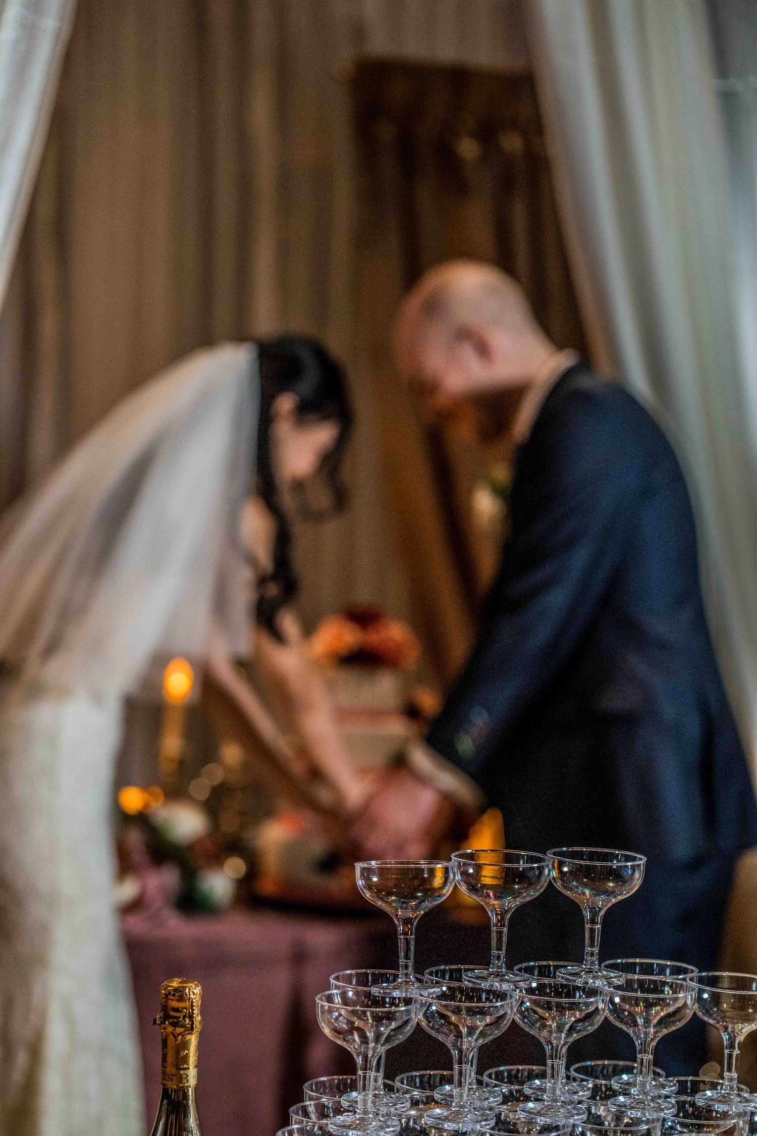 A champagne tower display at an elegant wedding with cream curtains and romantic lighting.