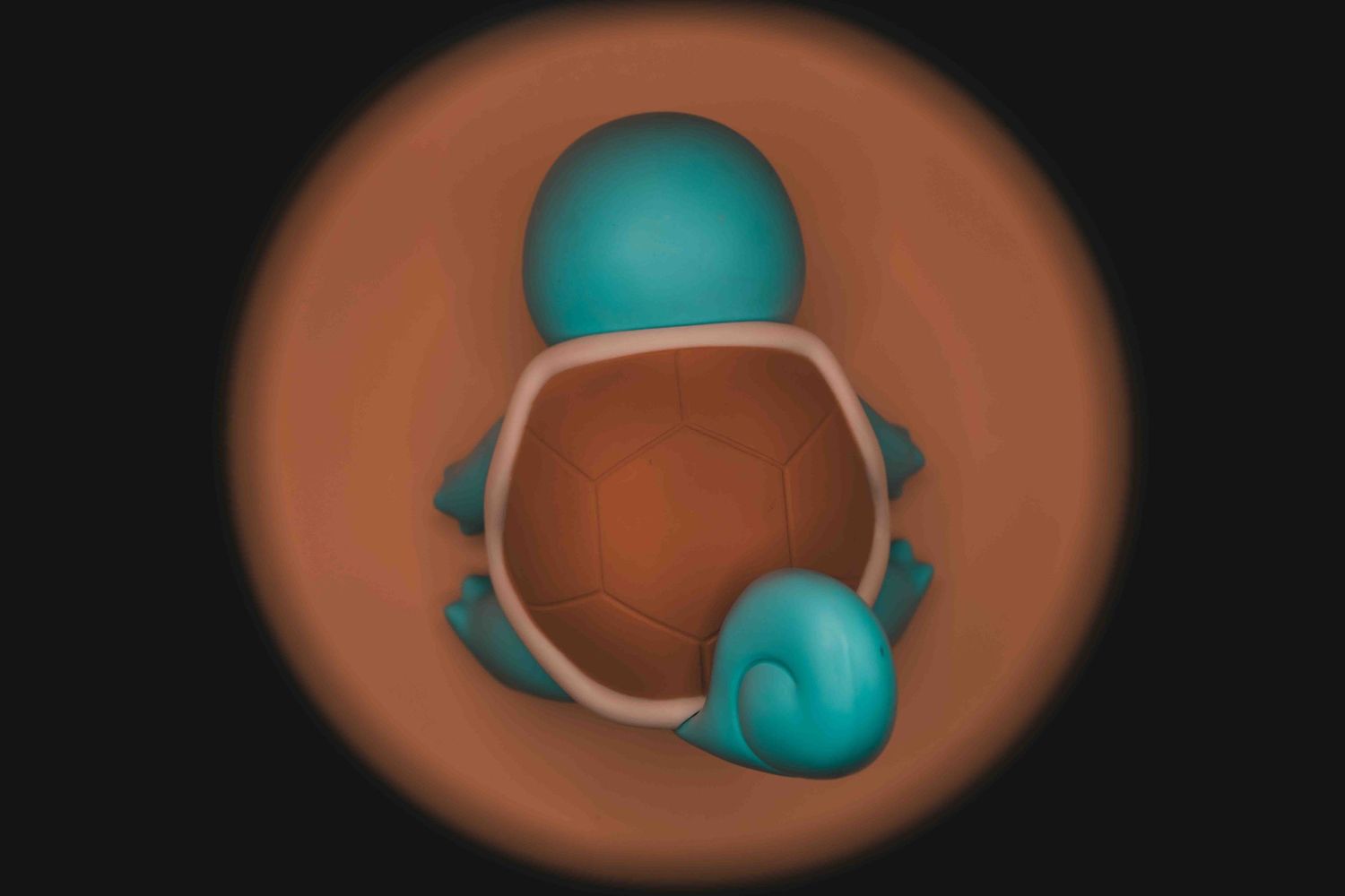 Top-down 3D render of Squirtle Pokemon figure with teal shell and body against warm brown vignette background.