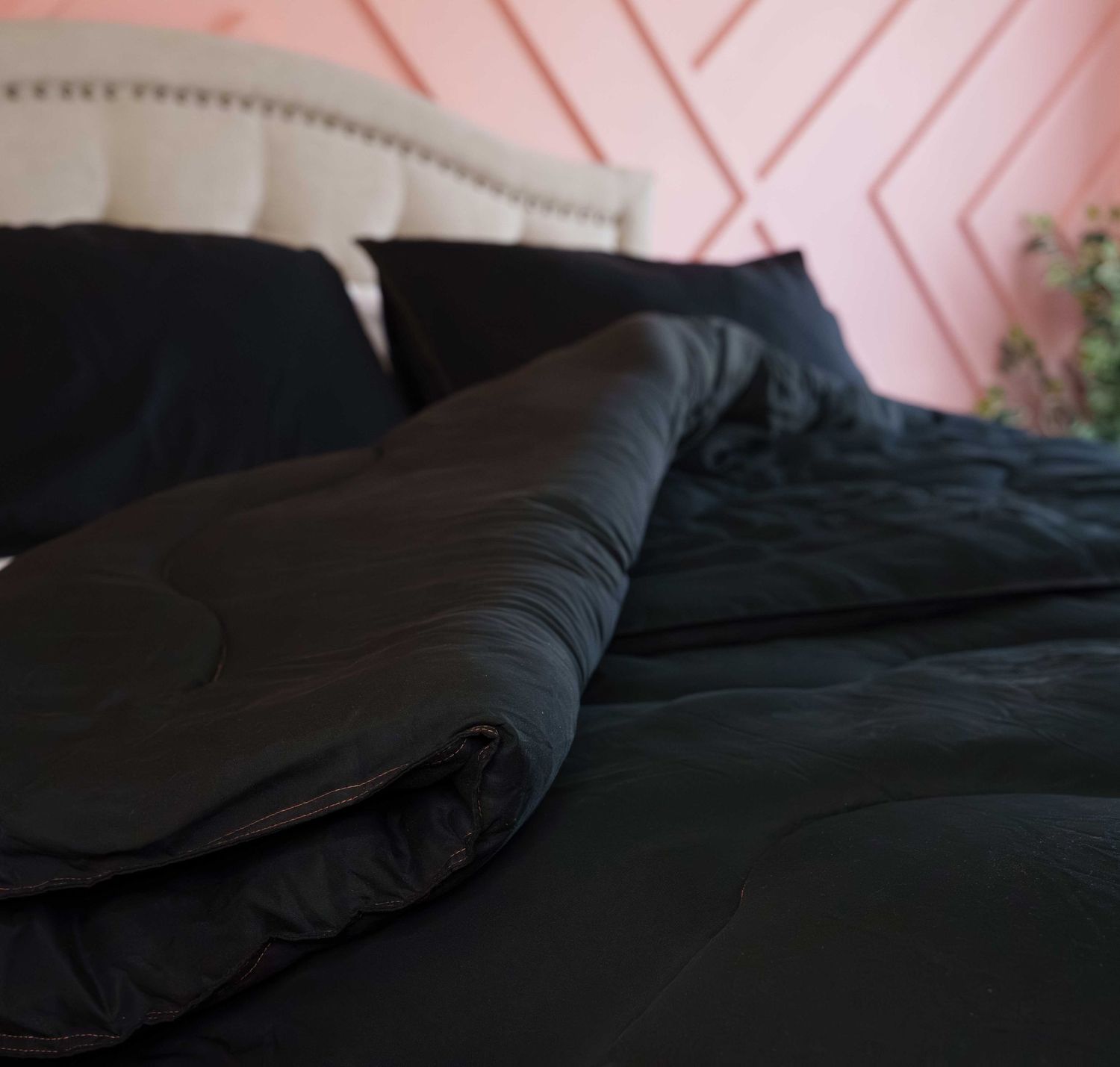 Black satin duvet cover folded on a bed with matching pillows against a pink geometric headboard wall.
