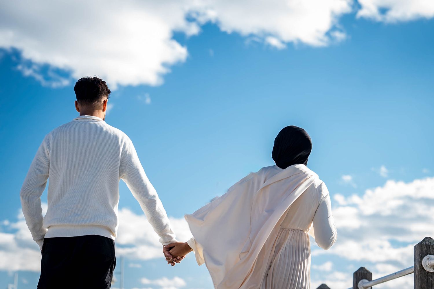 Silhouettes of people against a vibrant blue sky with white puffy clouds.