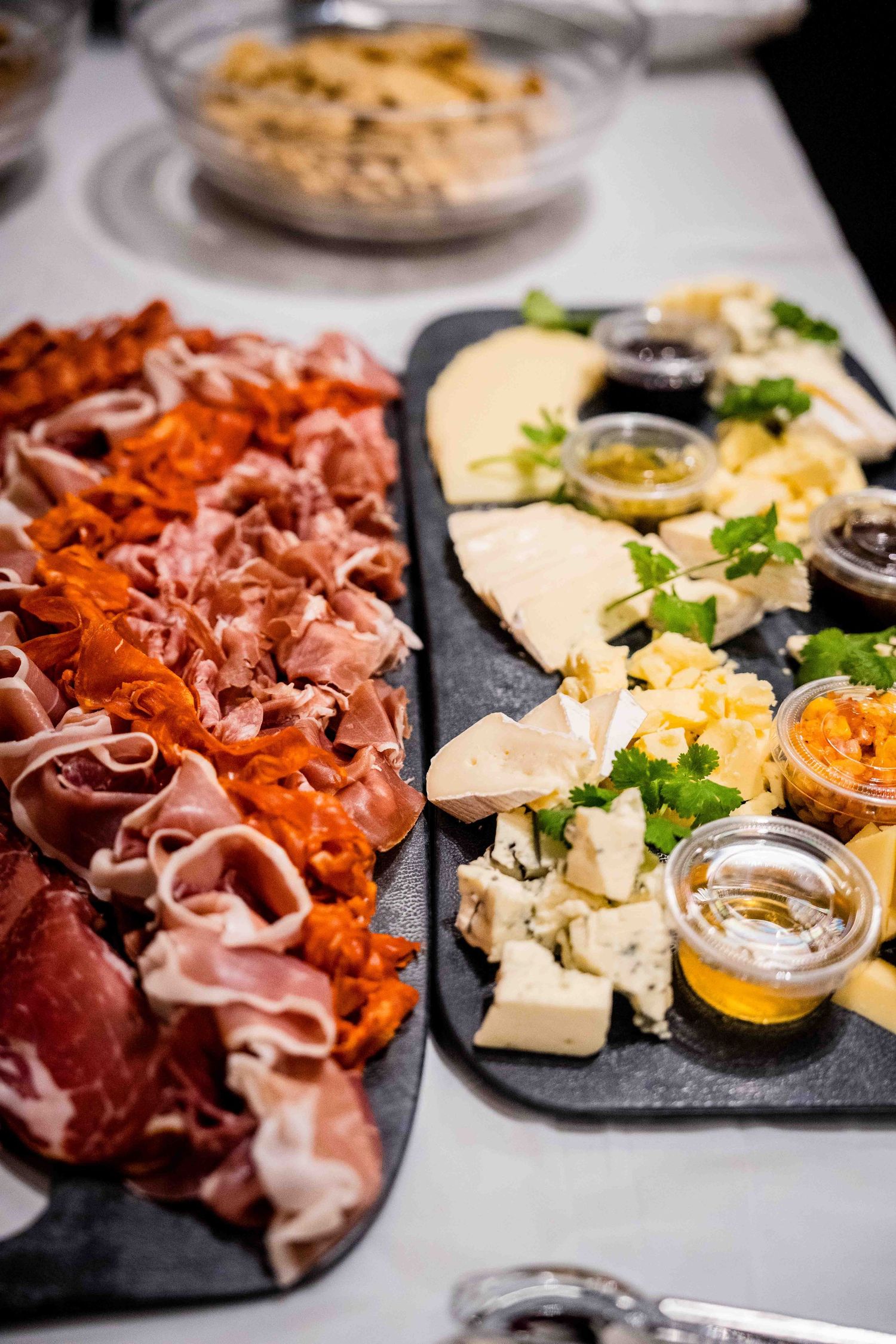 Charcuterie board with cured meats, cheeses, and honey served on black slate platters.