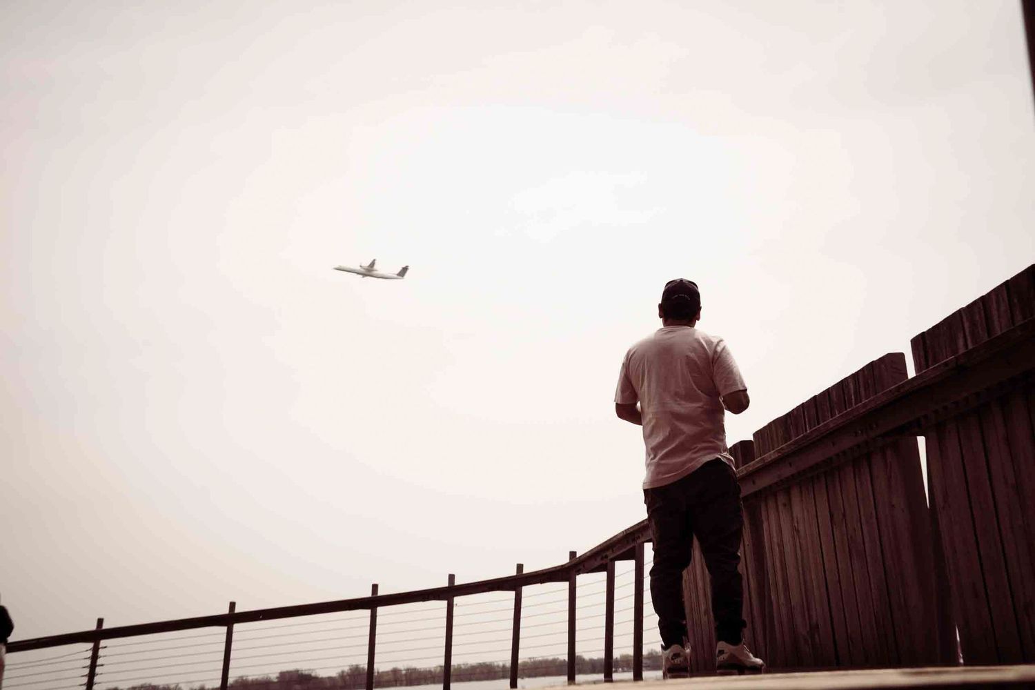 Silhouette figures watching airplane in distance from observation deck.