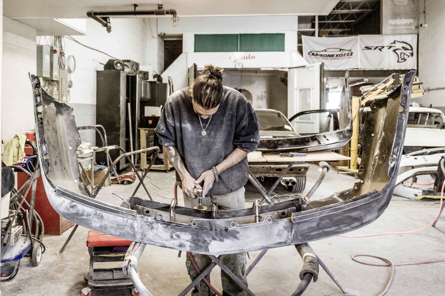 Auto technician working on a car bumper in a repair shop.