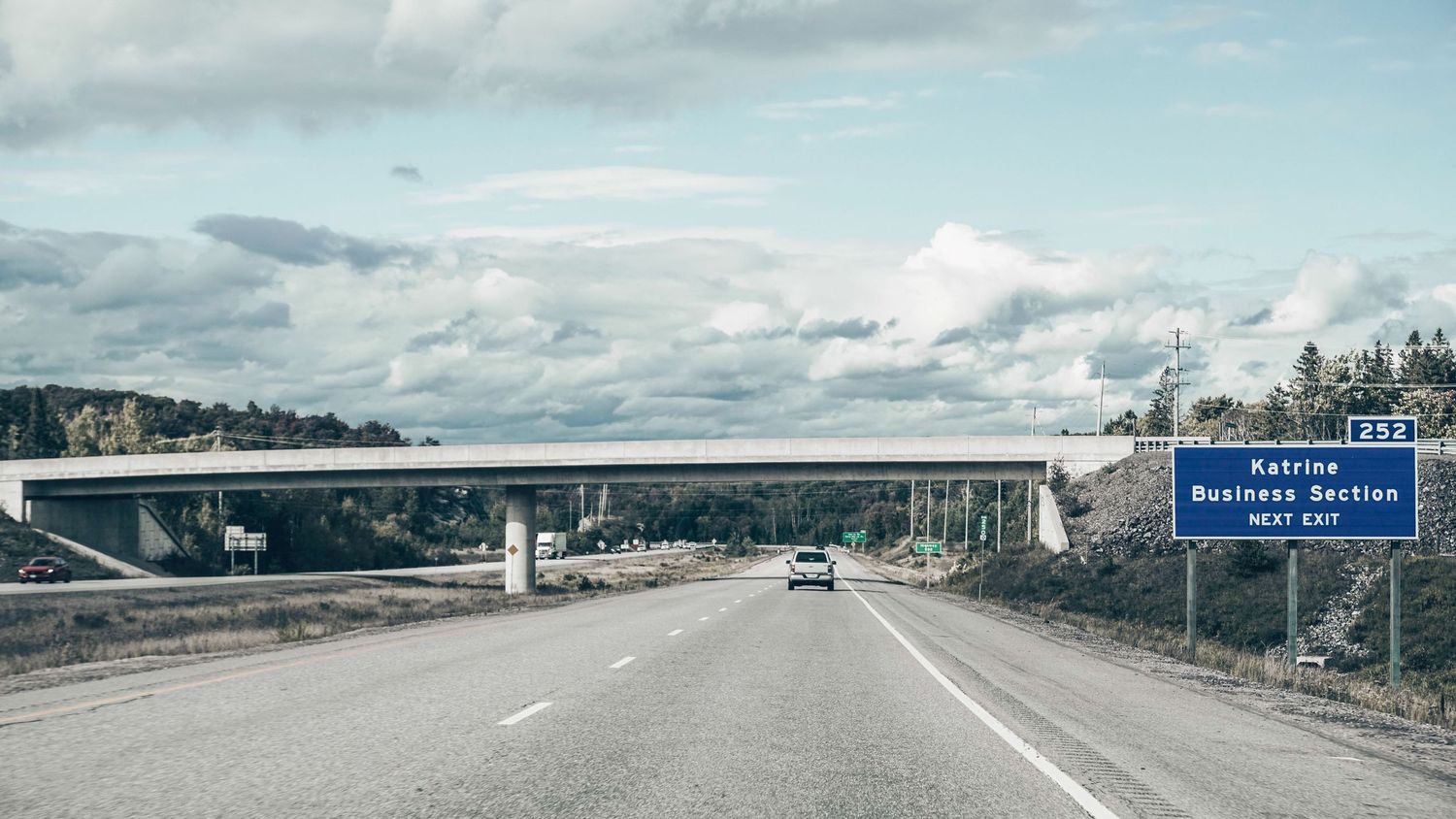 Wide highway stretching across a scenic landscape with mountains and clouds in the distance.