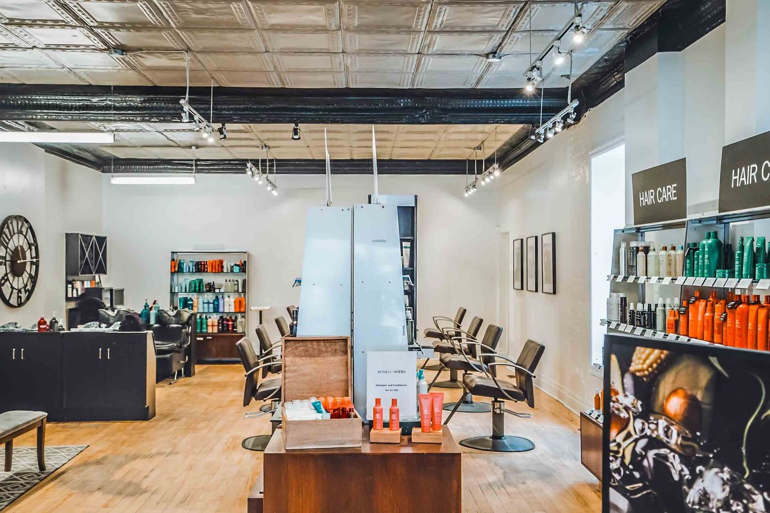 Modern hair salon interior with styling chairs, hair care products display, and industrial ceiling in a bright, open space.