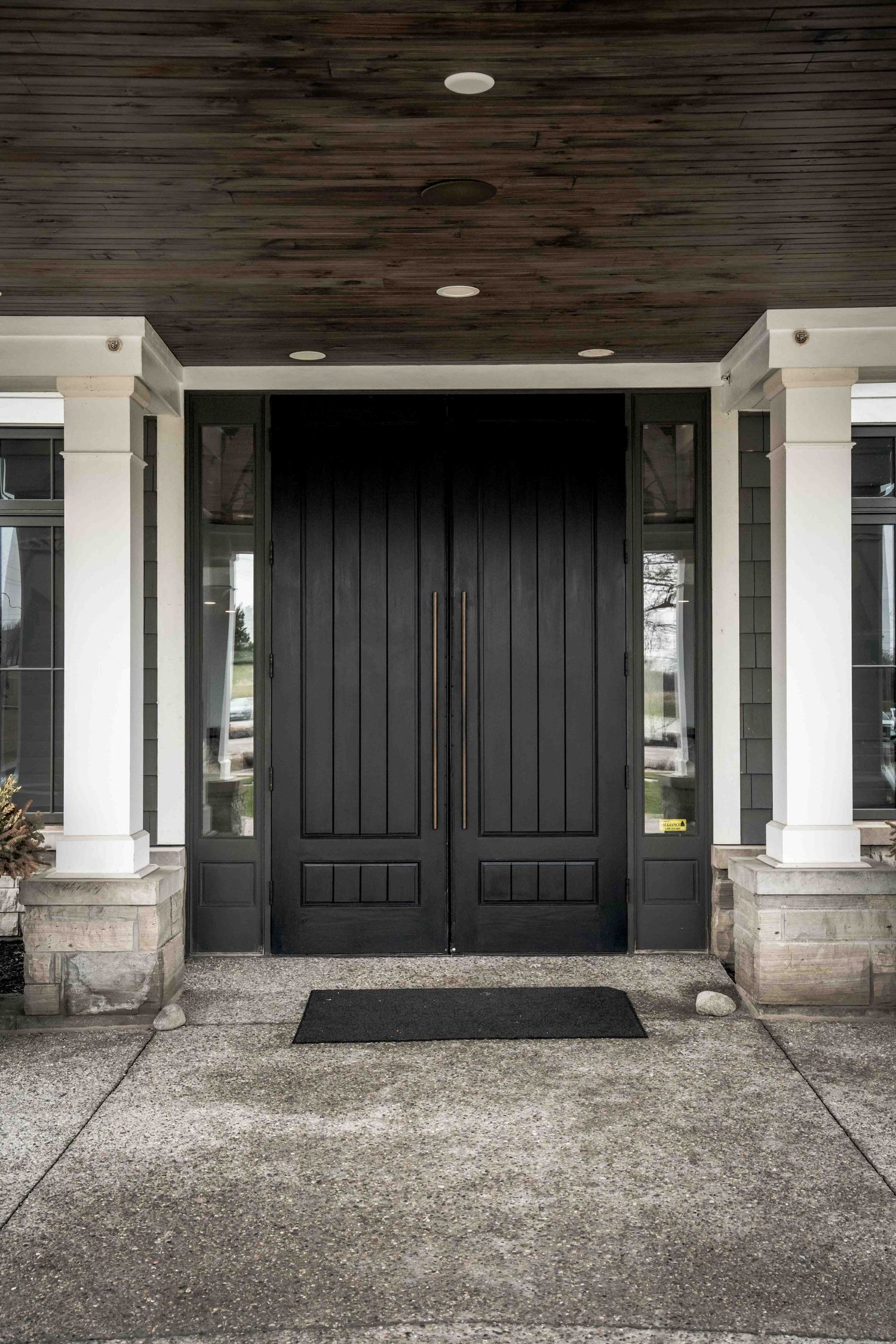 Elegant black double front door with sidelights, white columns, and dark wood ceiling on a covered porch entrance.