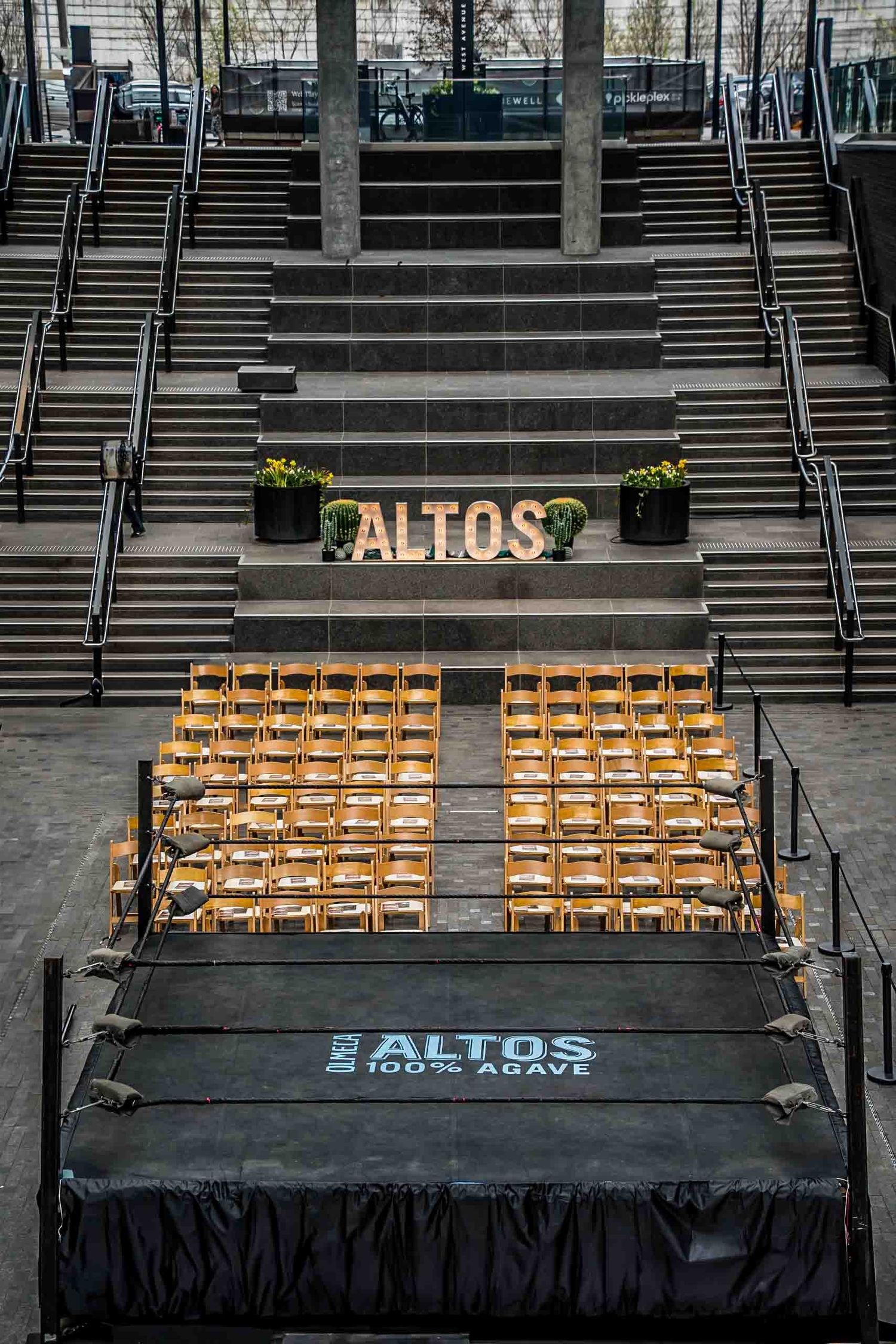 Empty amphitheater seating with Altos branded stage setup and wooden chairs.