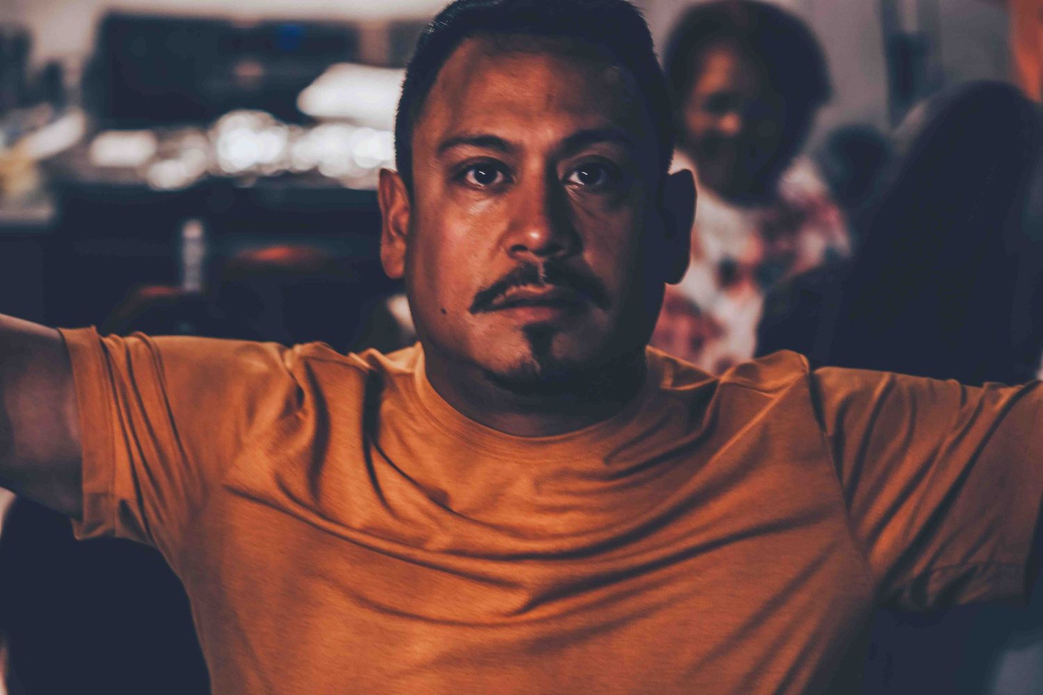 Person in orange hoodie showing various expressions in moody indoor lighting.