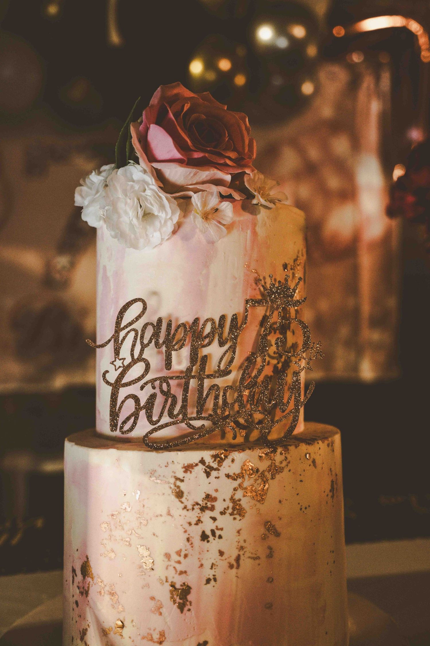 Elegant white and pink birthday cake decorated with gold accents and a 'Happy Birthday' topper.