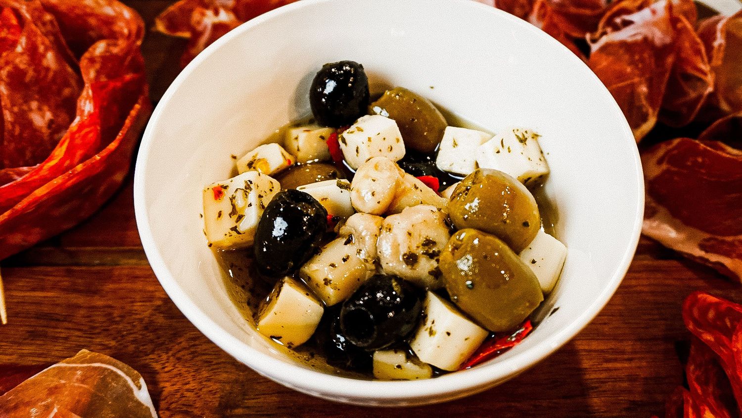 Mediterranean appetizer platter featuring marinated olives and cheese cubes in white ceramic bowls.
