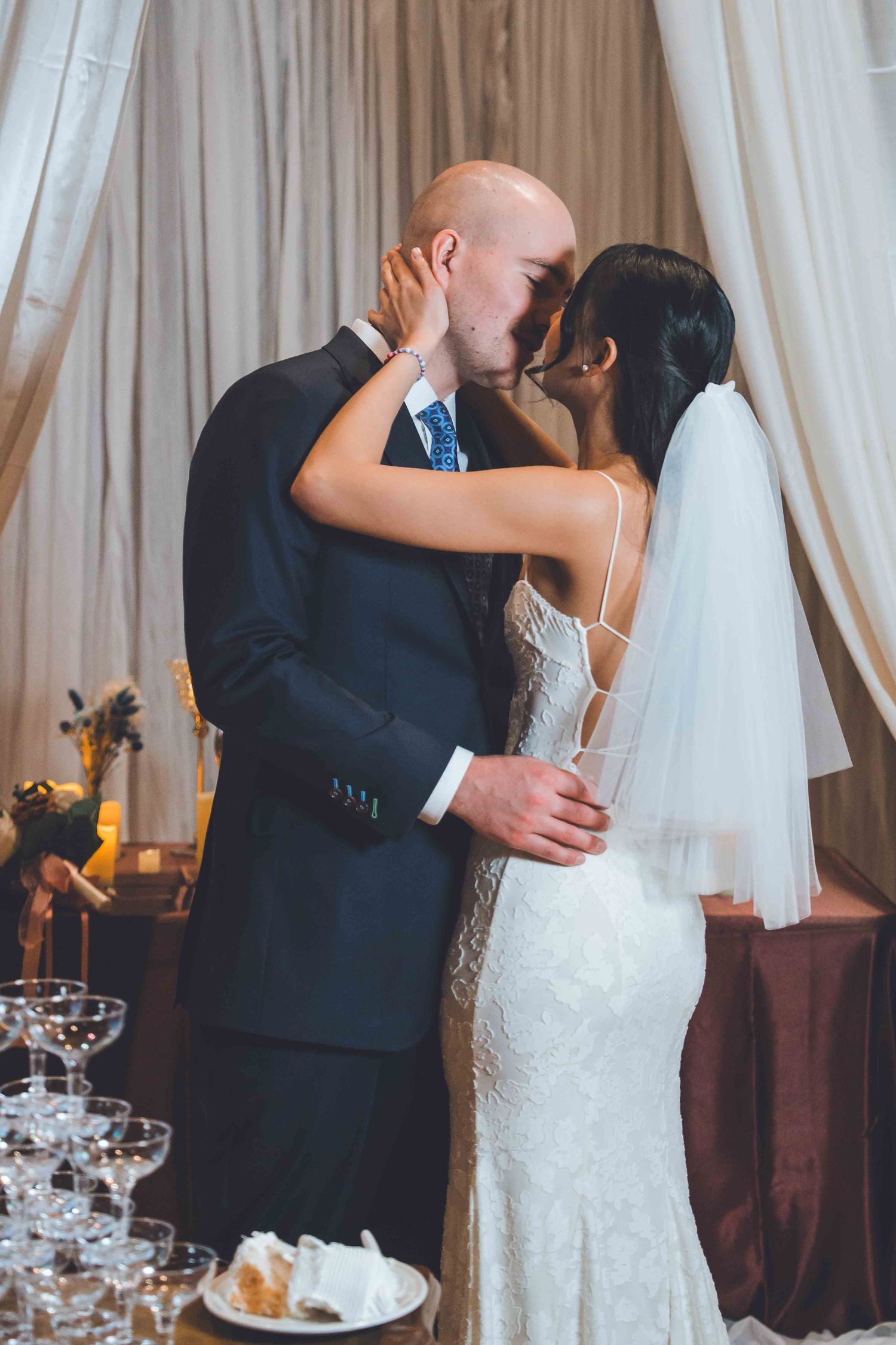 Wedding couple sharing intimate moments in front of white curtains at reception.