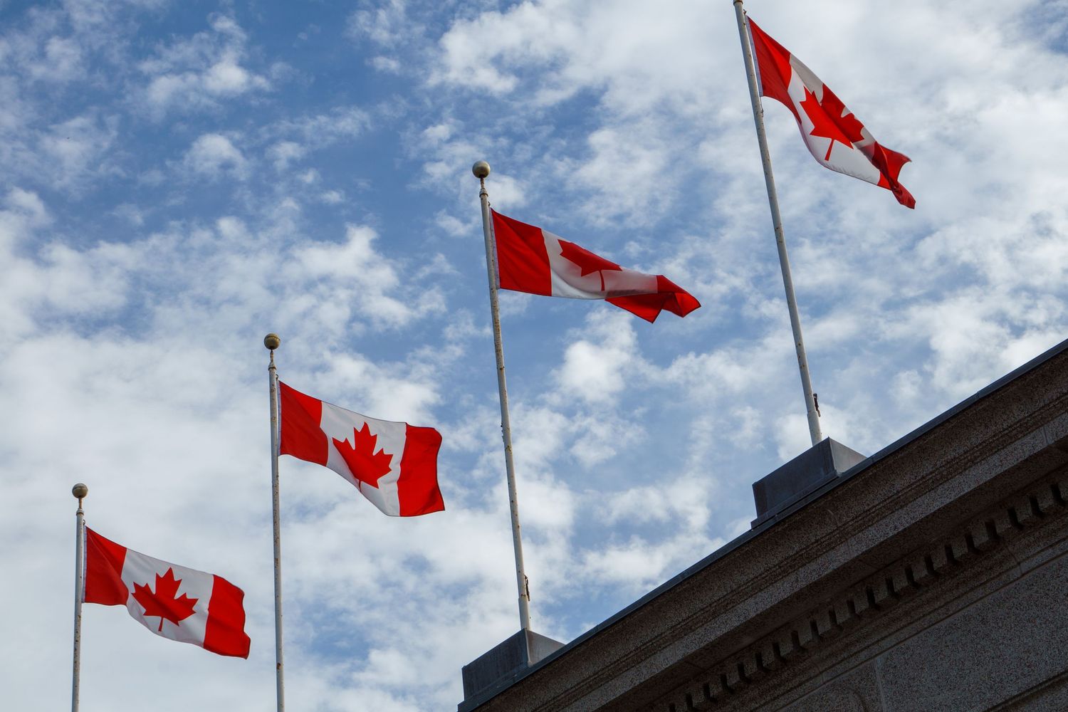 Three Canadian flags waving against a blue sky with white clouds.