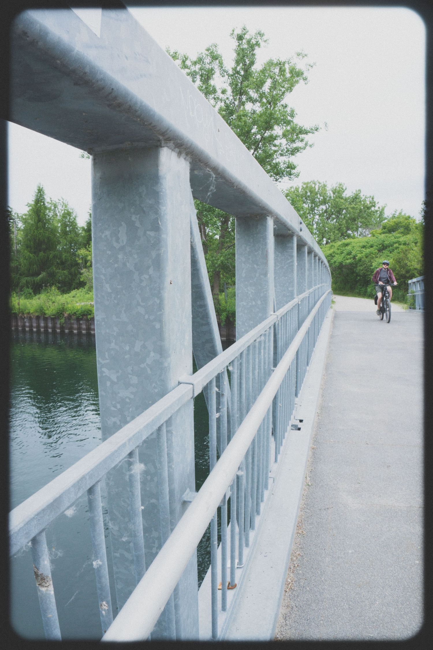 White metal railing along a waterfront path with water and trees visible.