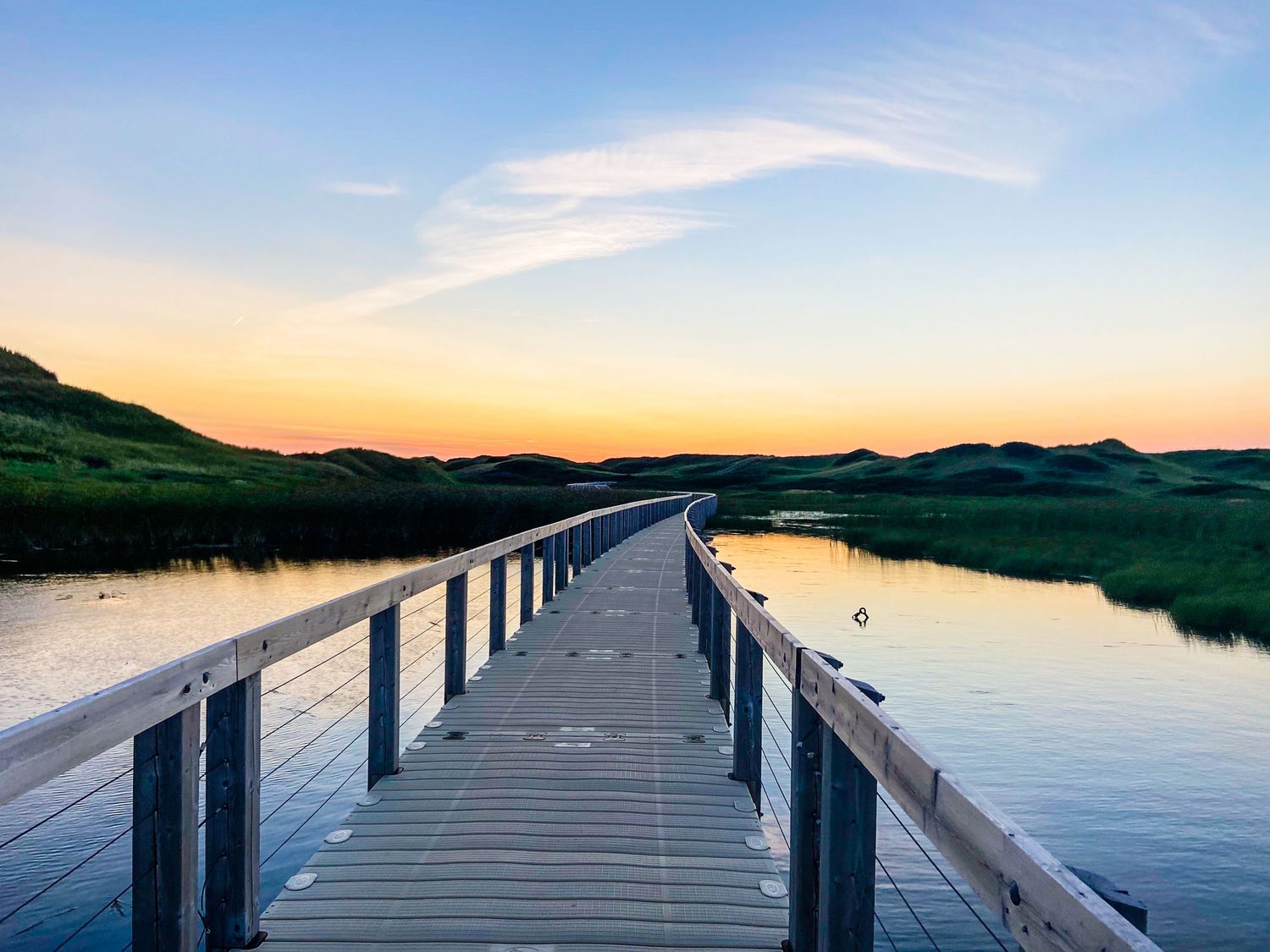 Wooden pier extending over calm waters during a peaceful sunset with golden sky.