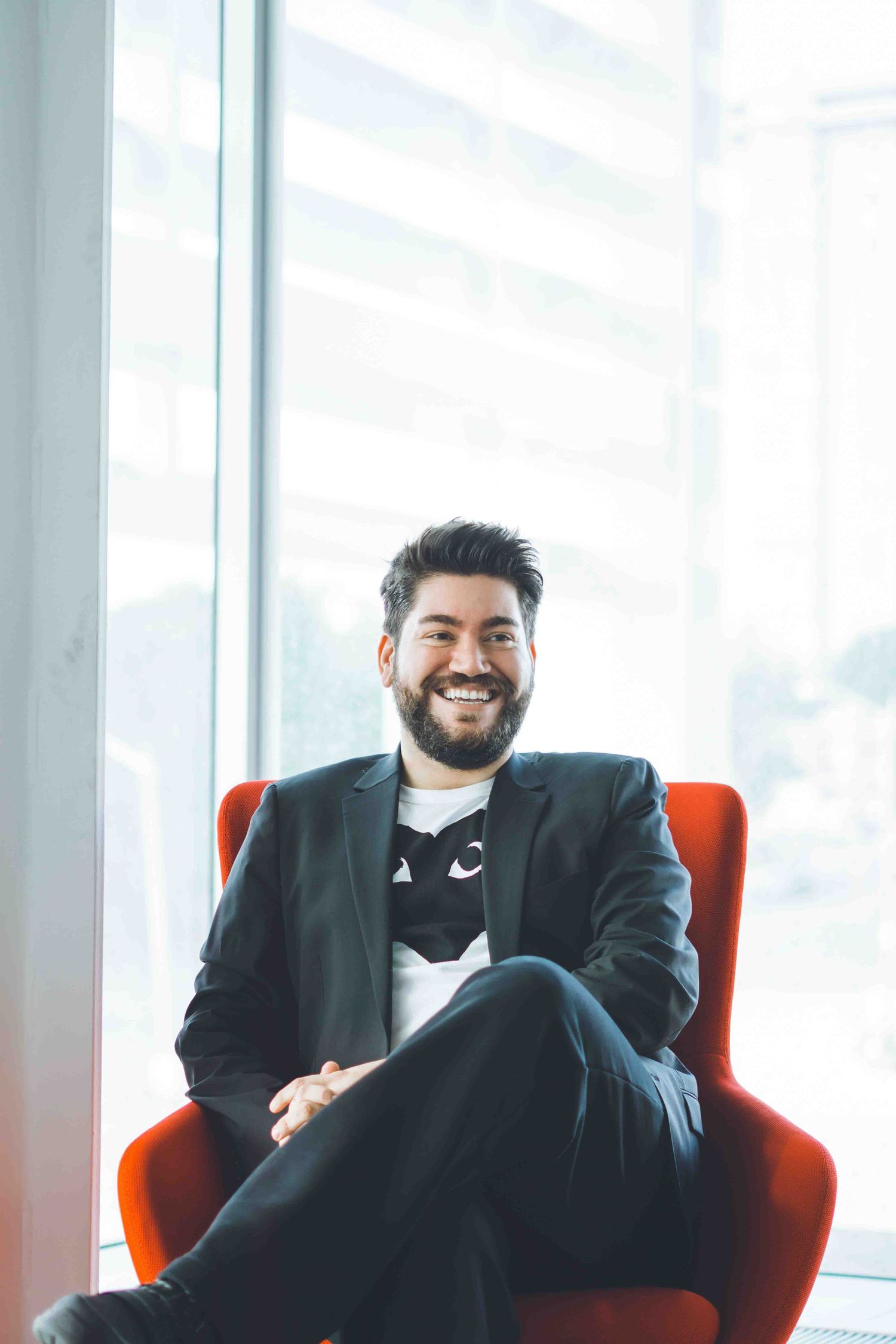 Professional in dark suit relaxing in bright modern office with red accent chairs.