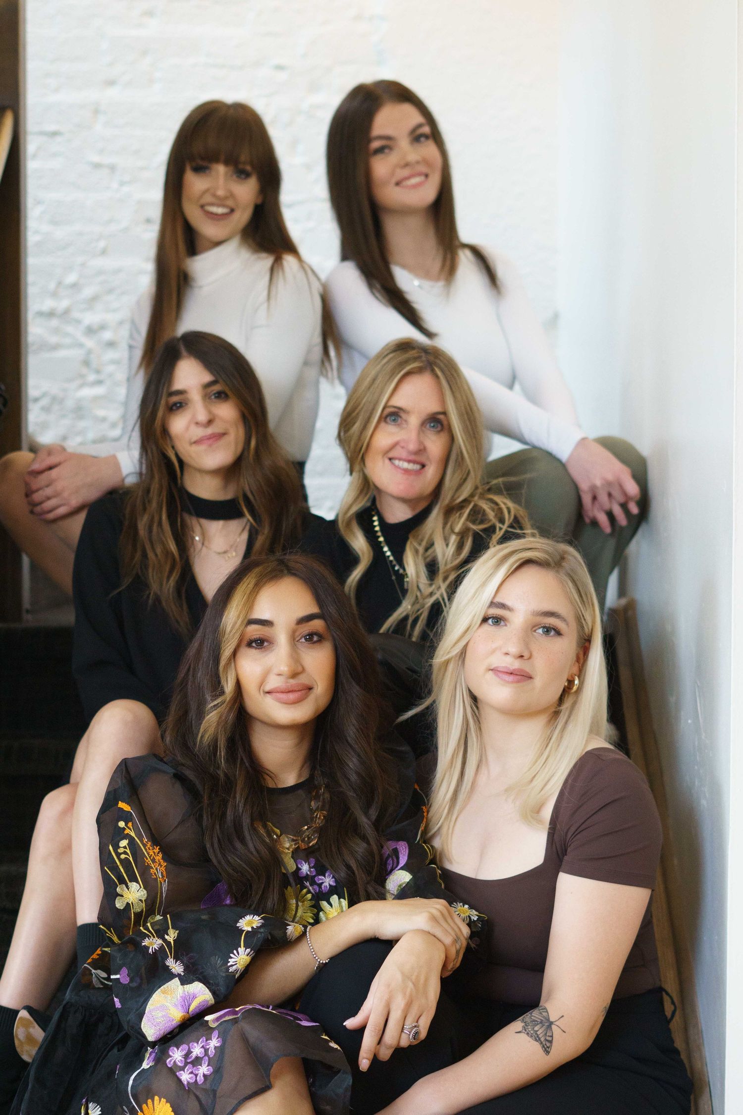 A group of women sitting together against a white wall in casual attire.