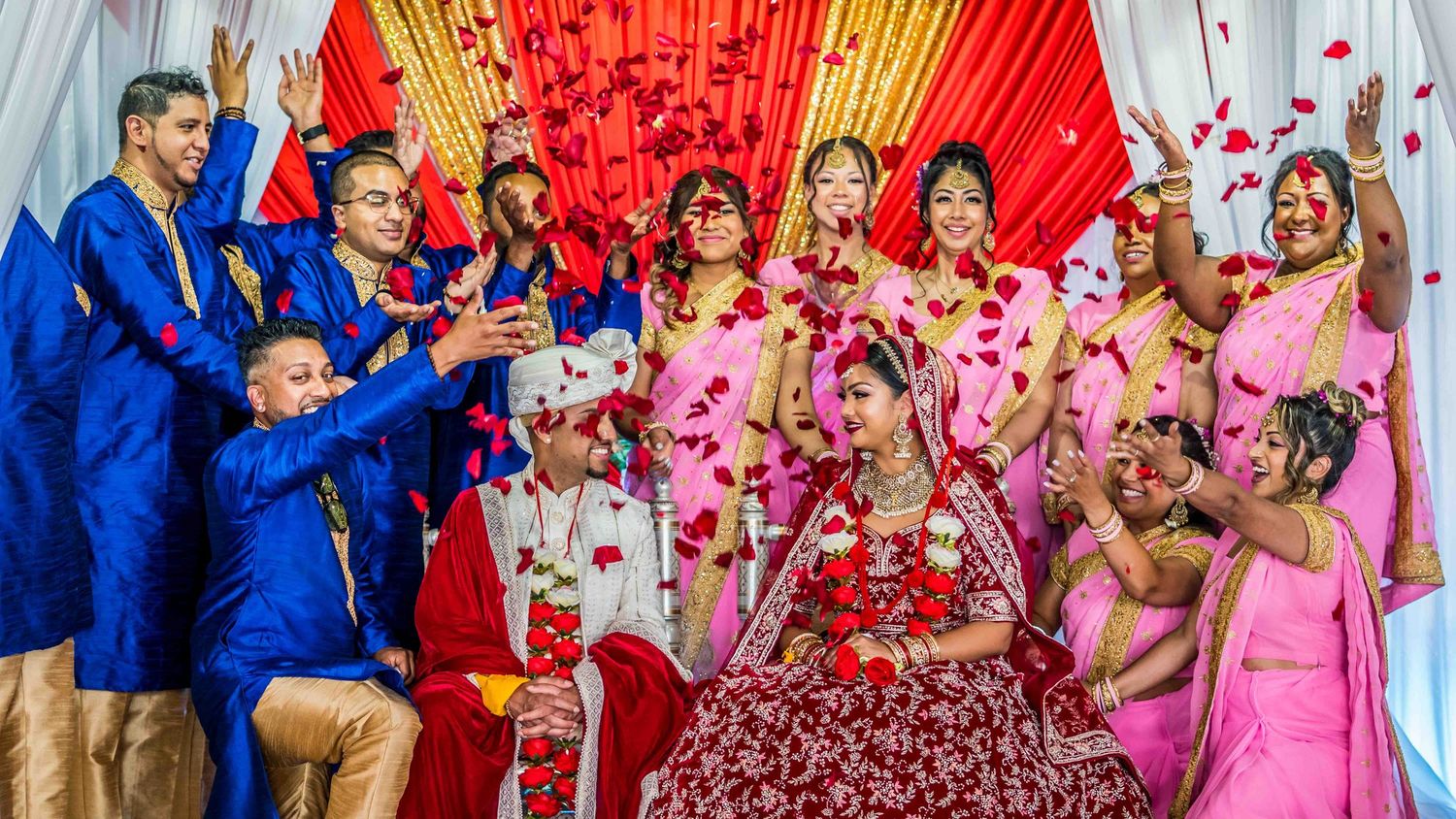 Festive celebration hall decorated with red and gold drapes and pink flower petals.