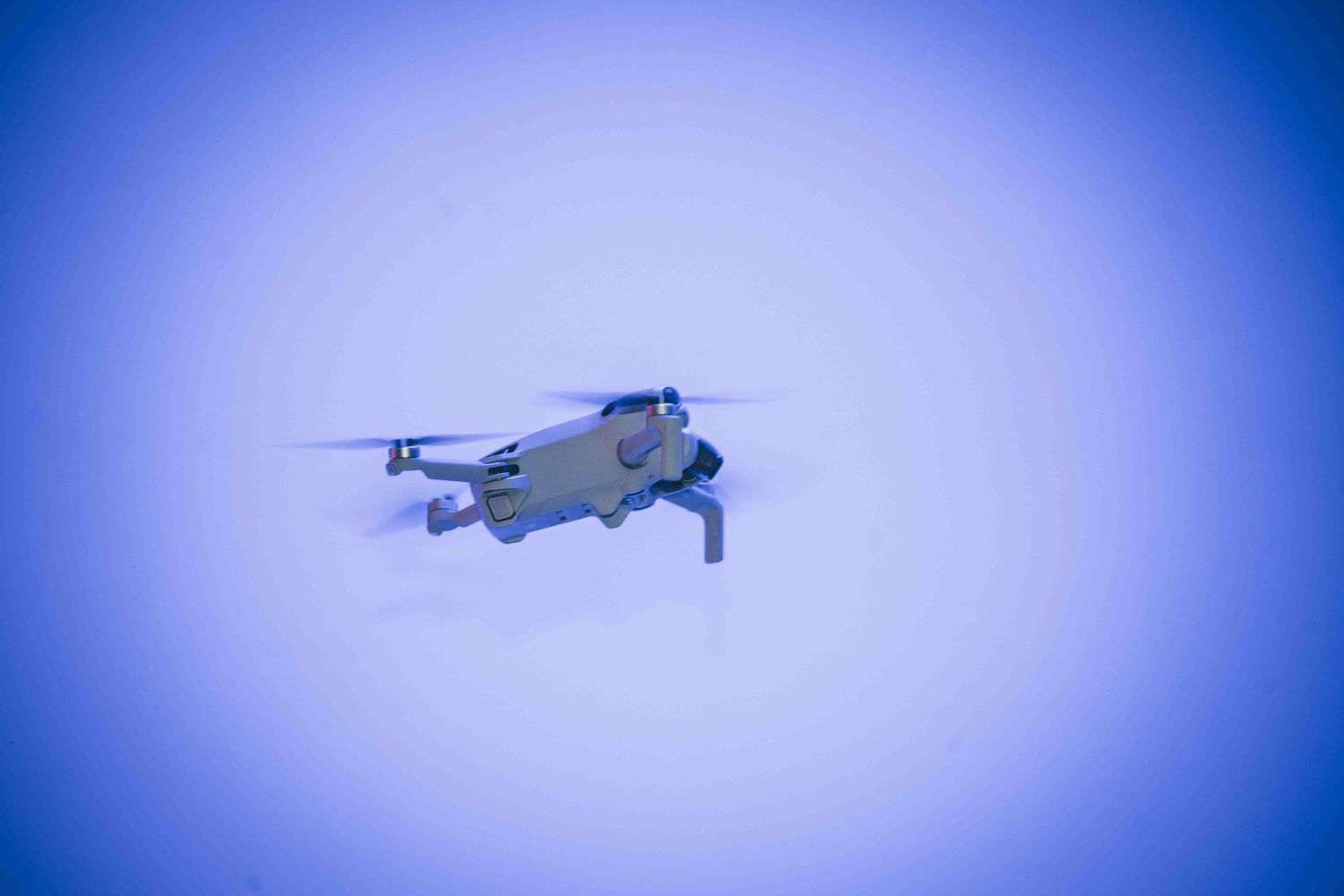 A drone flying in the sky against a bright blue background.