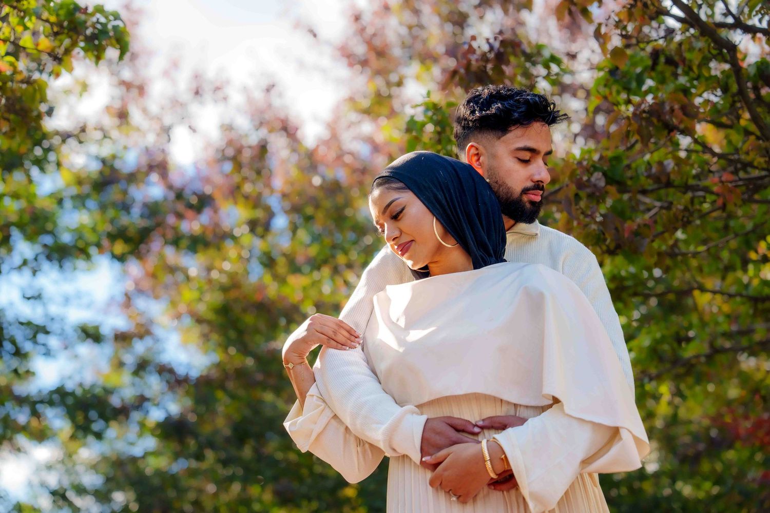 A couple embracing outdoors surrounded by autumn foliage and sunlight.