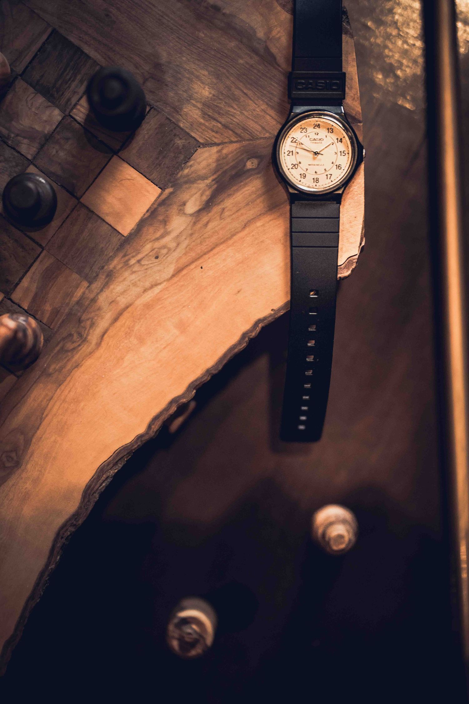 Black wristwatch with cream-colored face resting on wooden surface in moody lighting.