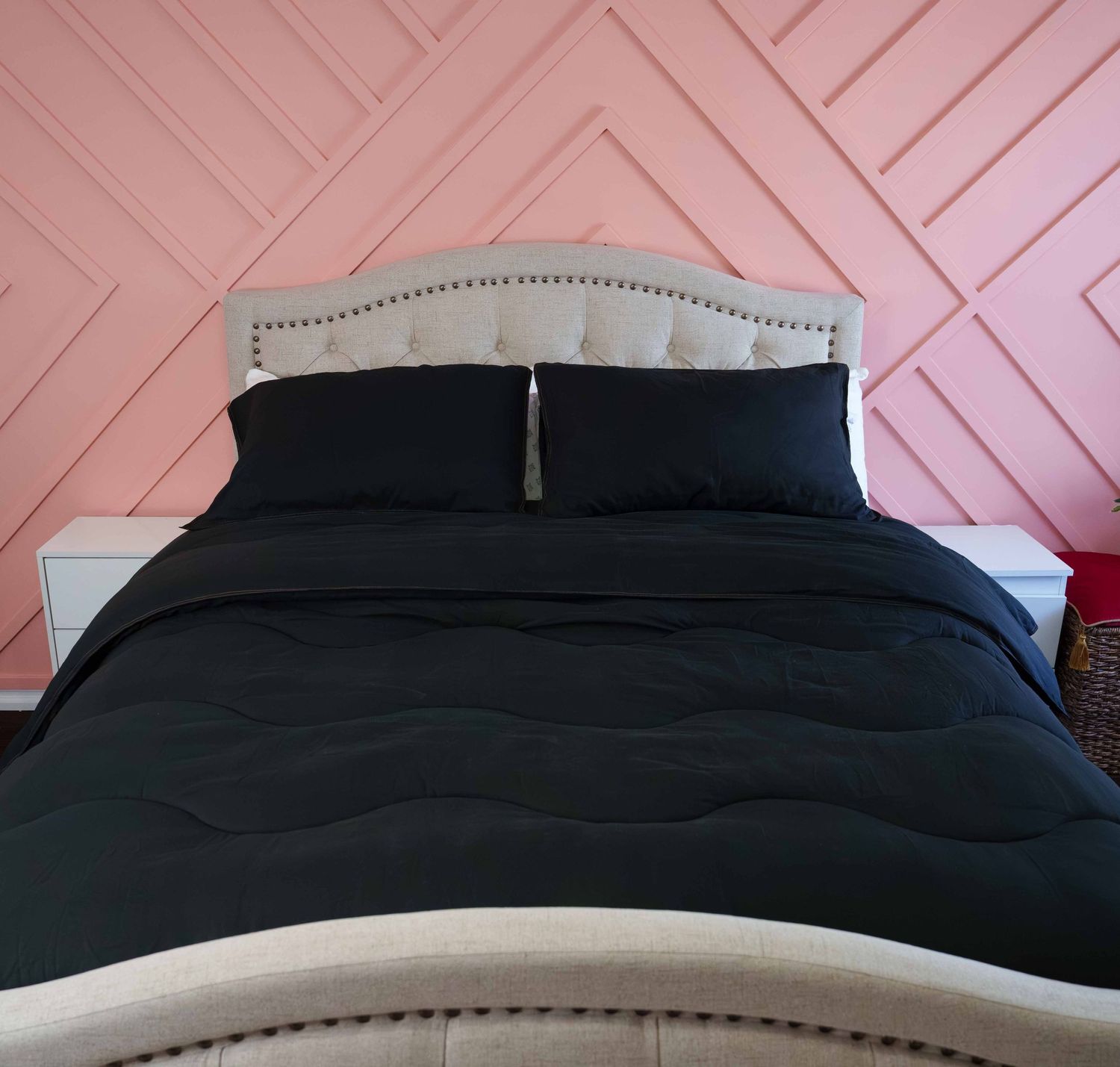 Black comforter set on a bed with matching pillowcases, styled against a pink geometric accent wall.
