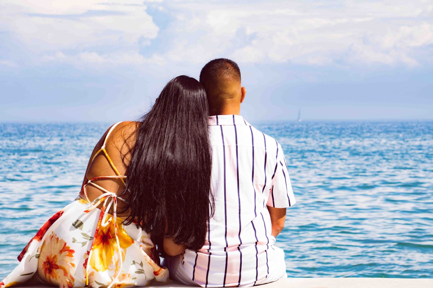 Couple sitting together by the ocean on a sunny day.