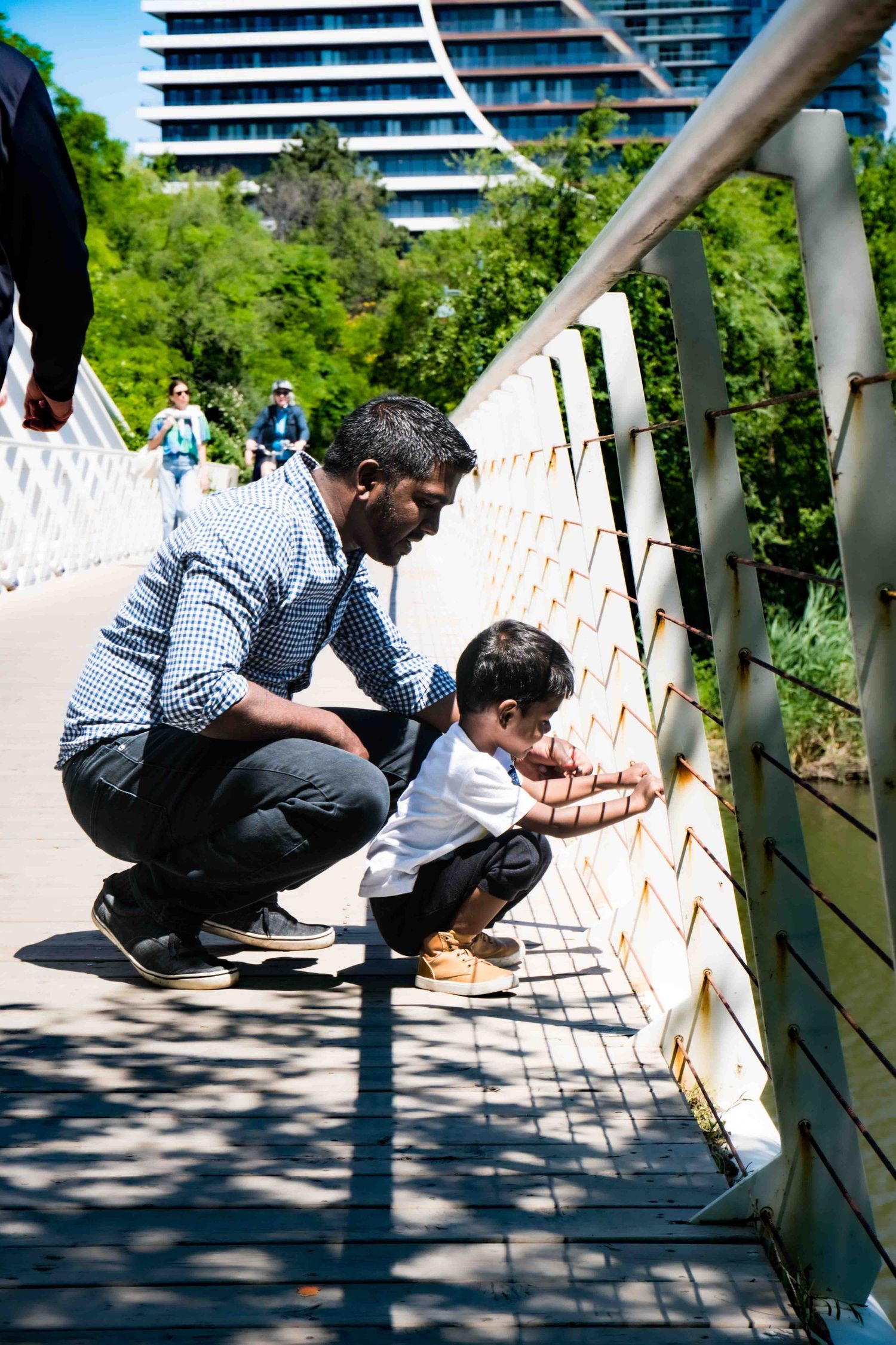 Two people examining details on a wooden bridge railing in bright sunlight.