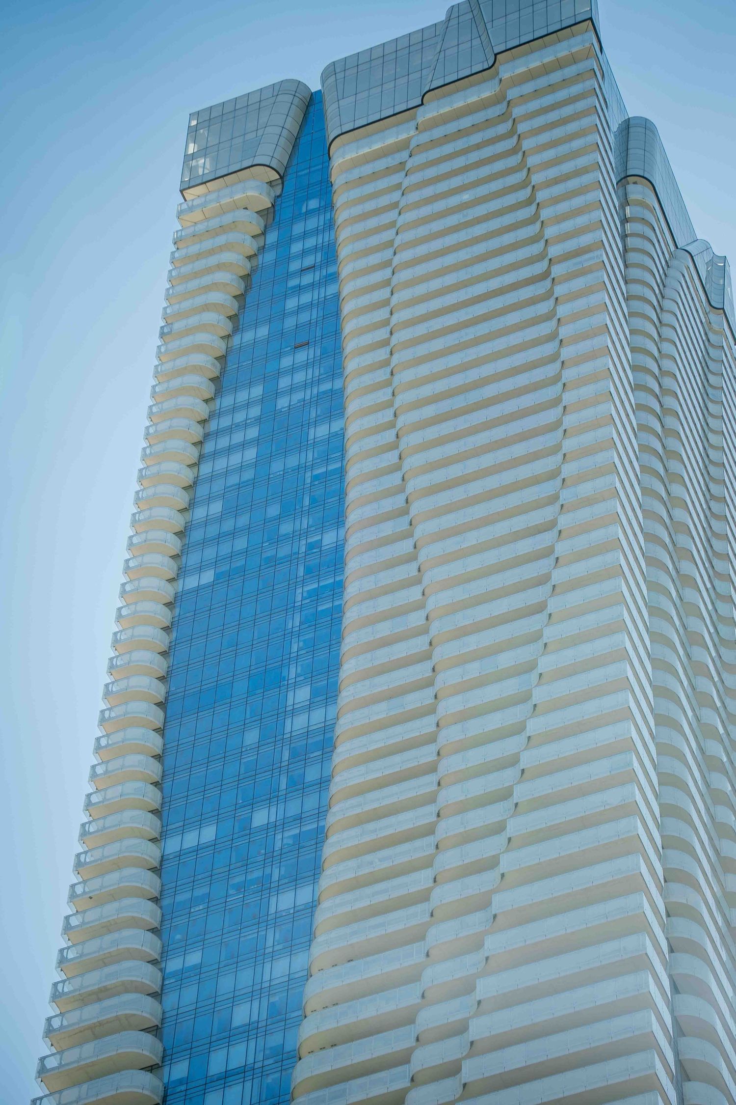 Modern high-rise building with alternating glass and concrete stripes against blue sky.