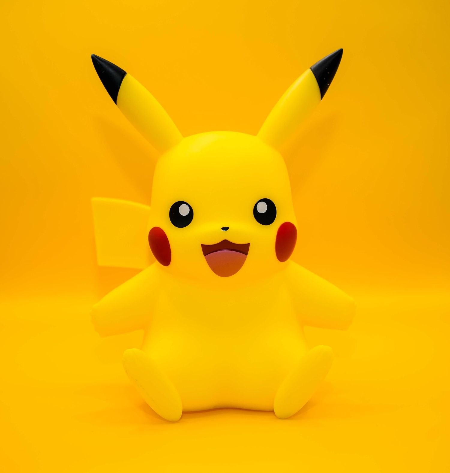 A bright yellow Pikachu Pokemon character figurine toy sitting against a vibrant yellow background.