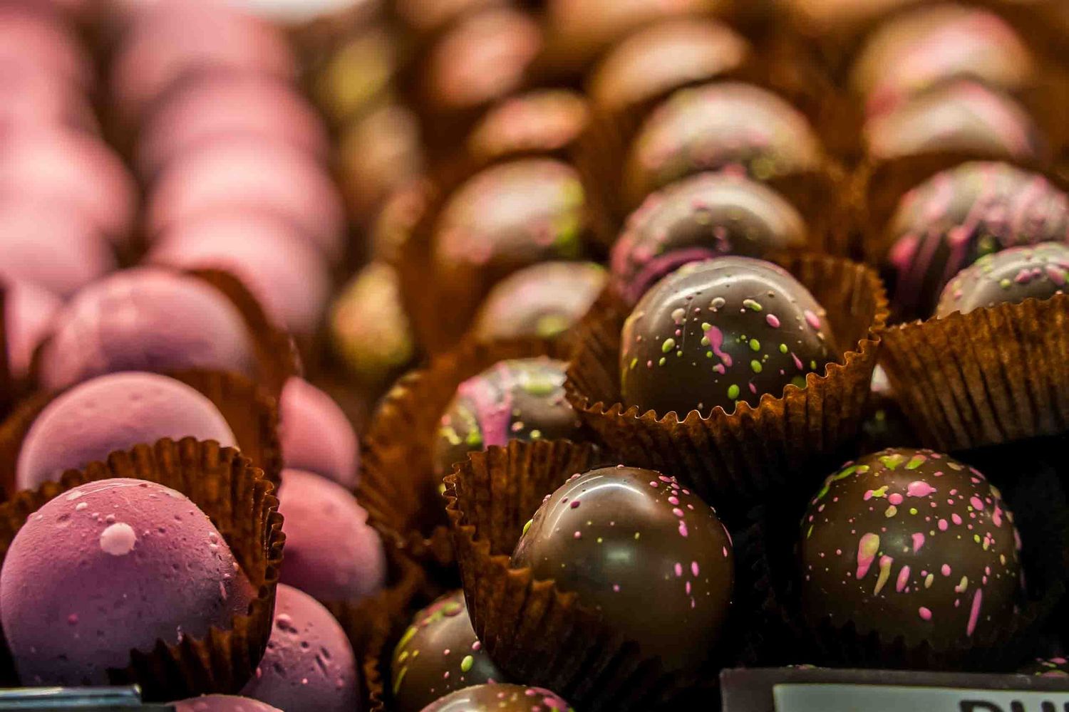 Macro shot of pink and brown chocolate bonbons with decorative patterns.